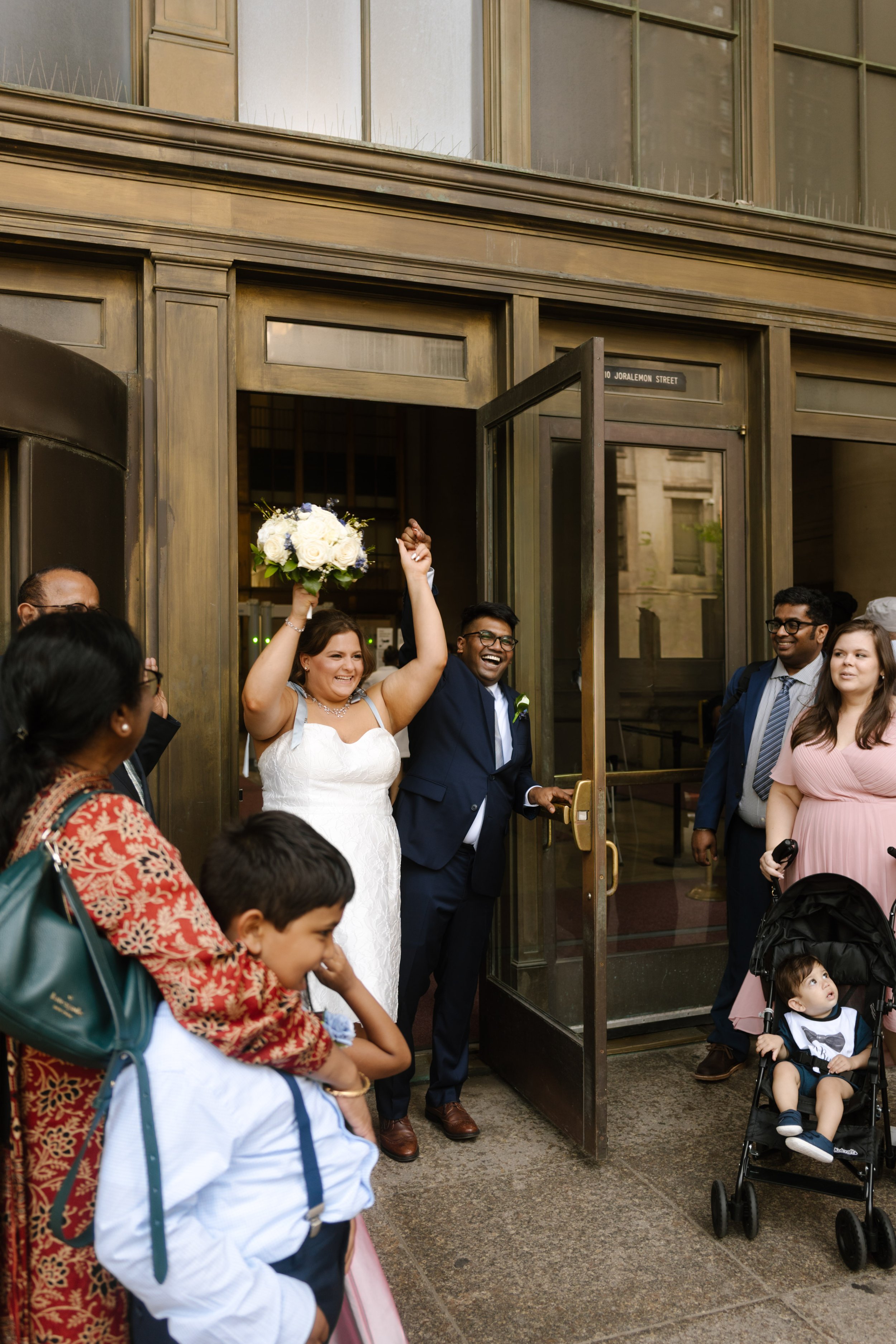 Newlyweds exit the courthouse surrounded by cheering family and friends after their Wedding Locations in NYC ceremony.
