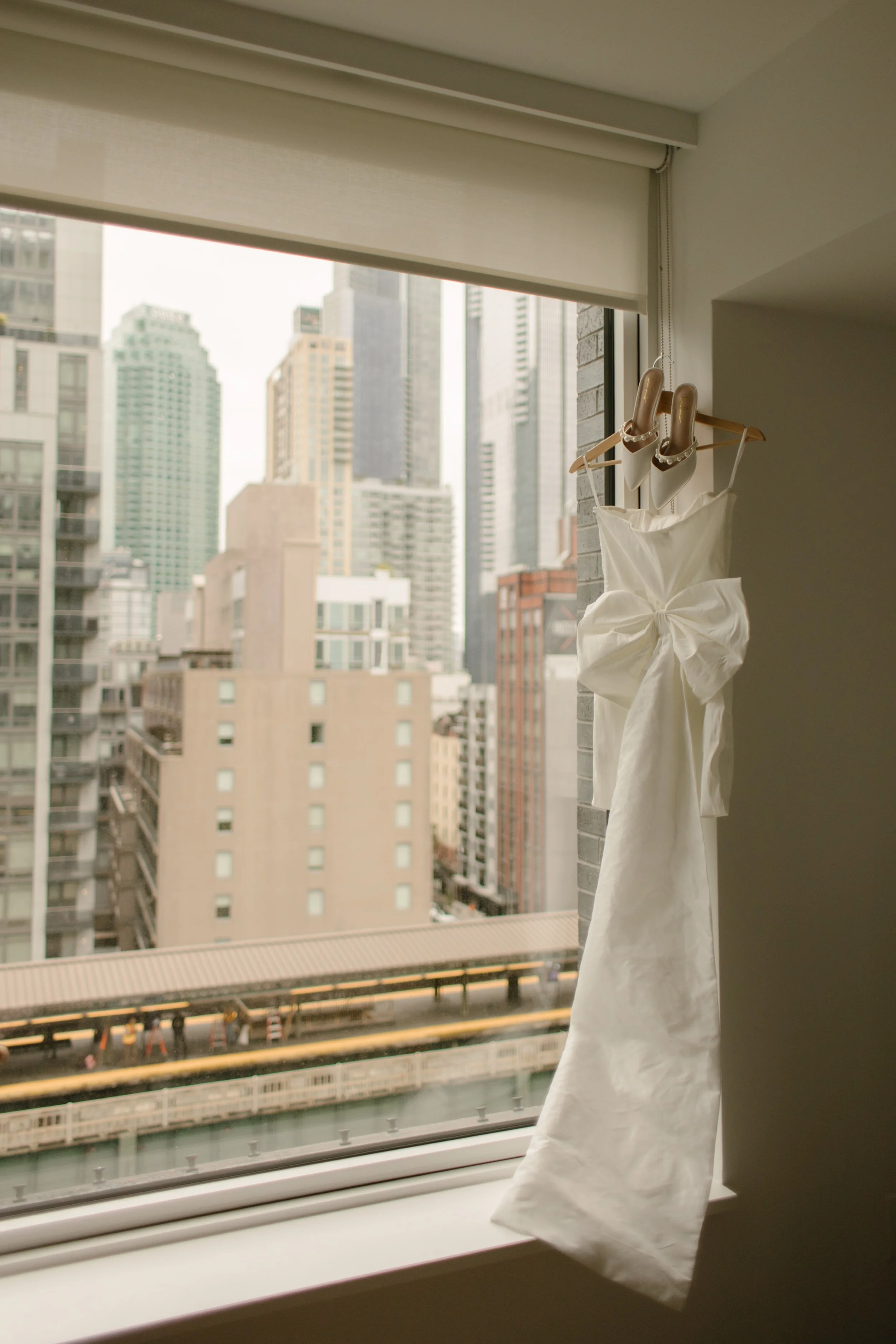 Wedding dress hanging in an apartment window overlooking the New York City skyline before an NYC courthouse wedding.