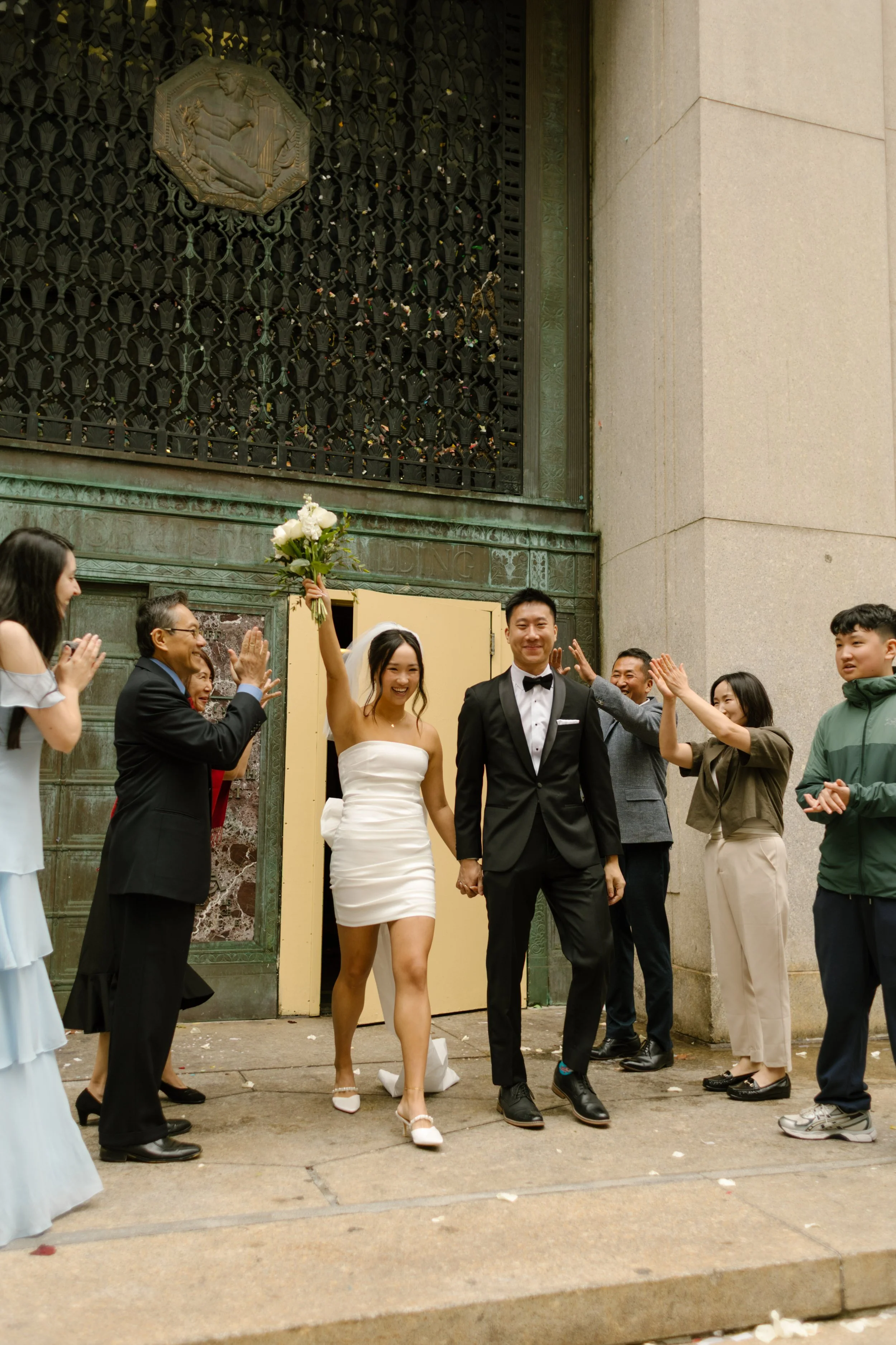 Bride and groom walking through the iconic yellow doors after their NYC courthouse wedding as family and friends cheer them on.