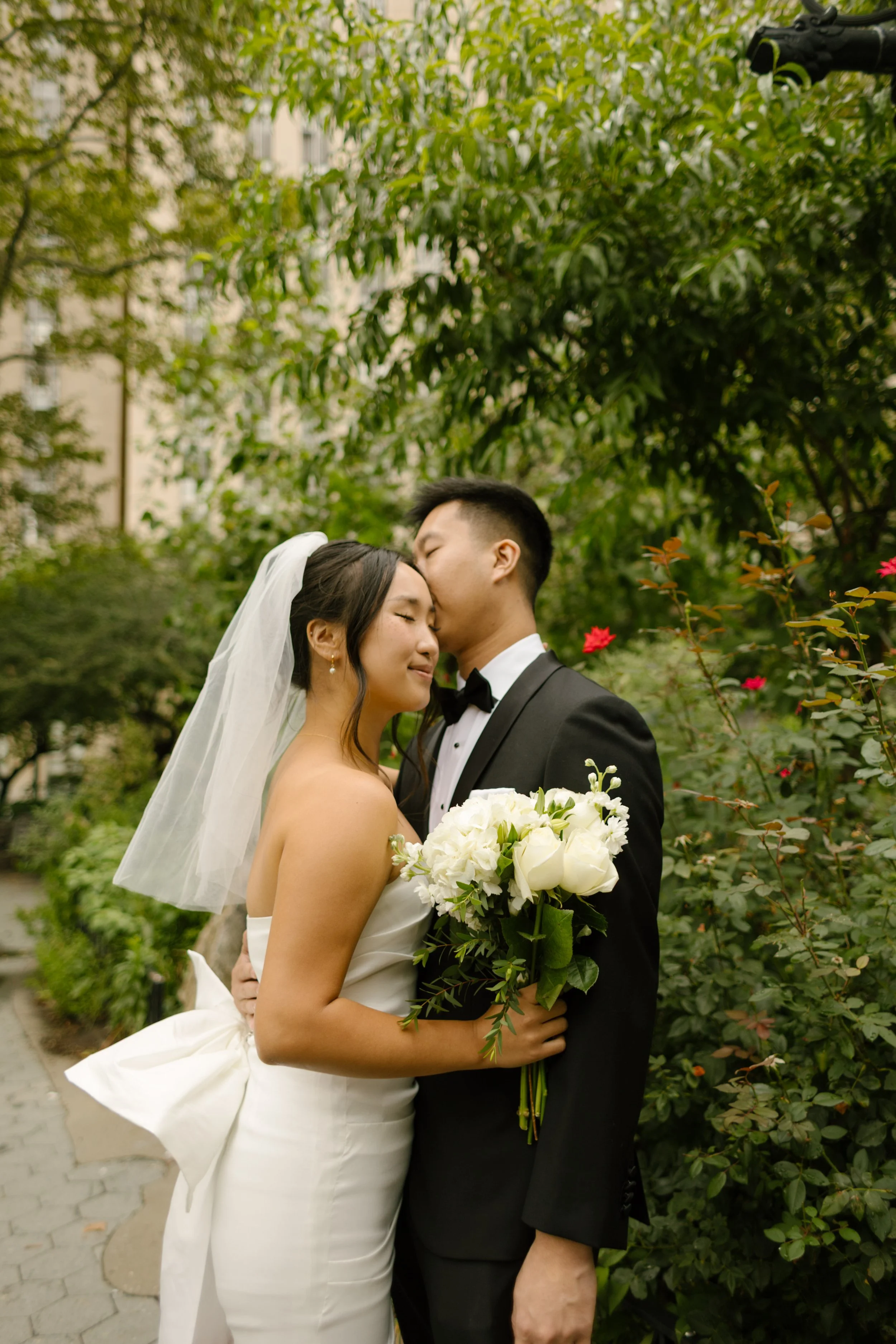 Romantic portrait of newlyweds embracing in a garden after their NYC courthouse wedding, surrounded by lush greenery and white roses.