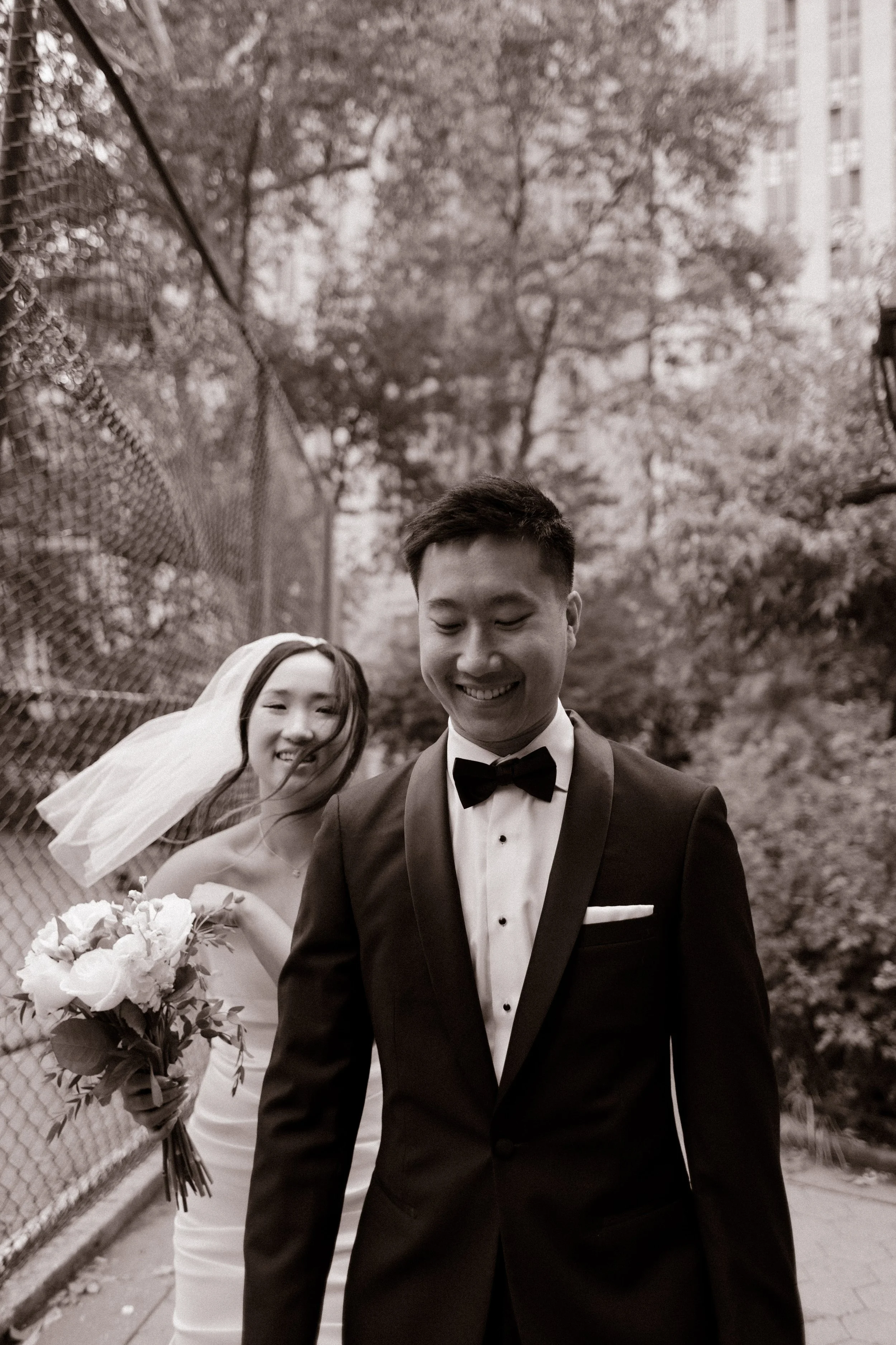 Black-and-white portrait of a bride and groom walking together through a quiet New York City street after their wedding ceremony.