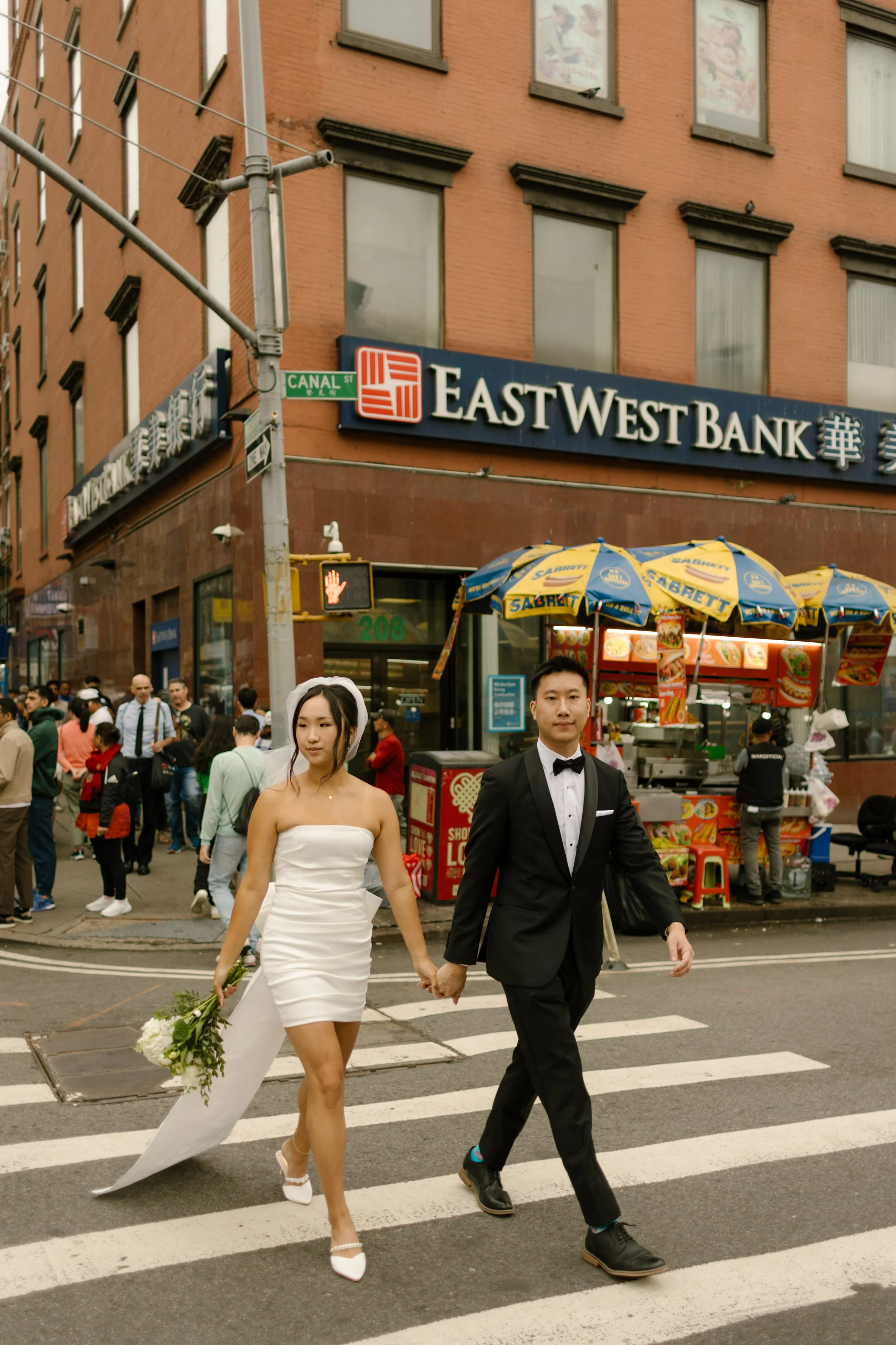 Bride and groom crossing a Chinatown crosswalk after their NYC courthouse wedding, surrounded by the vibrant energy of New York City.