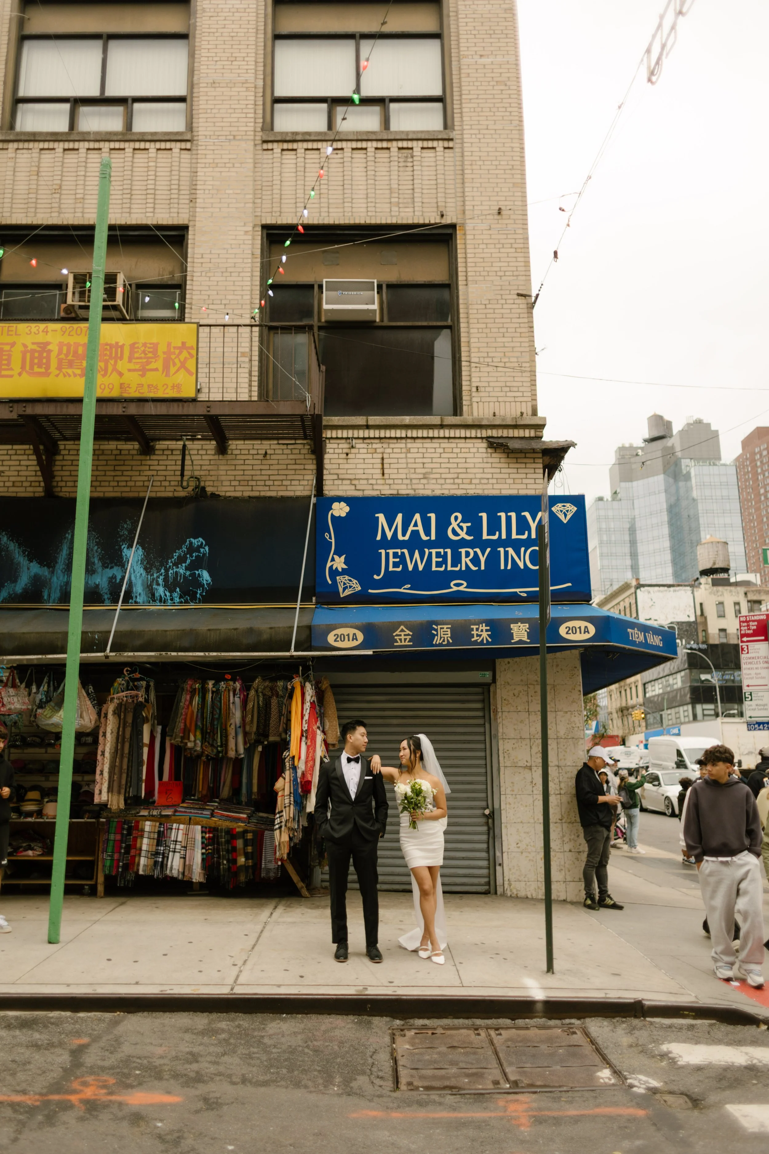Newlyweds standing together on a Chinatown sidewalk surrounded by colorful storefronts and the energy of New York City.