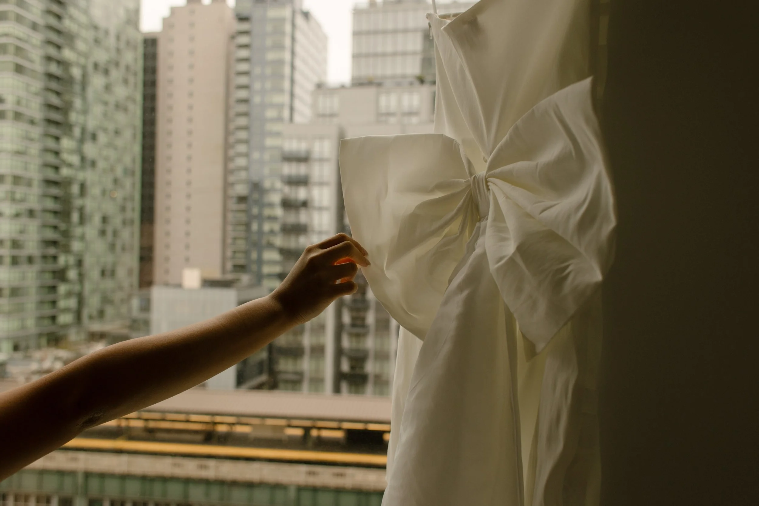 Bride reaching for her wedding dress hanging in an apartment window before an NYC courthouse wedding.