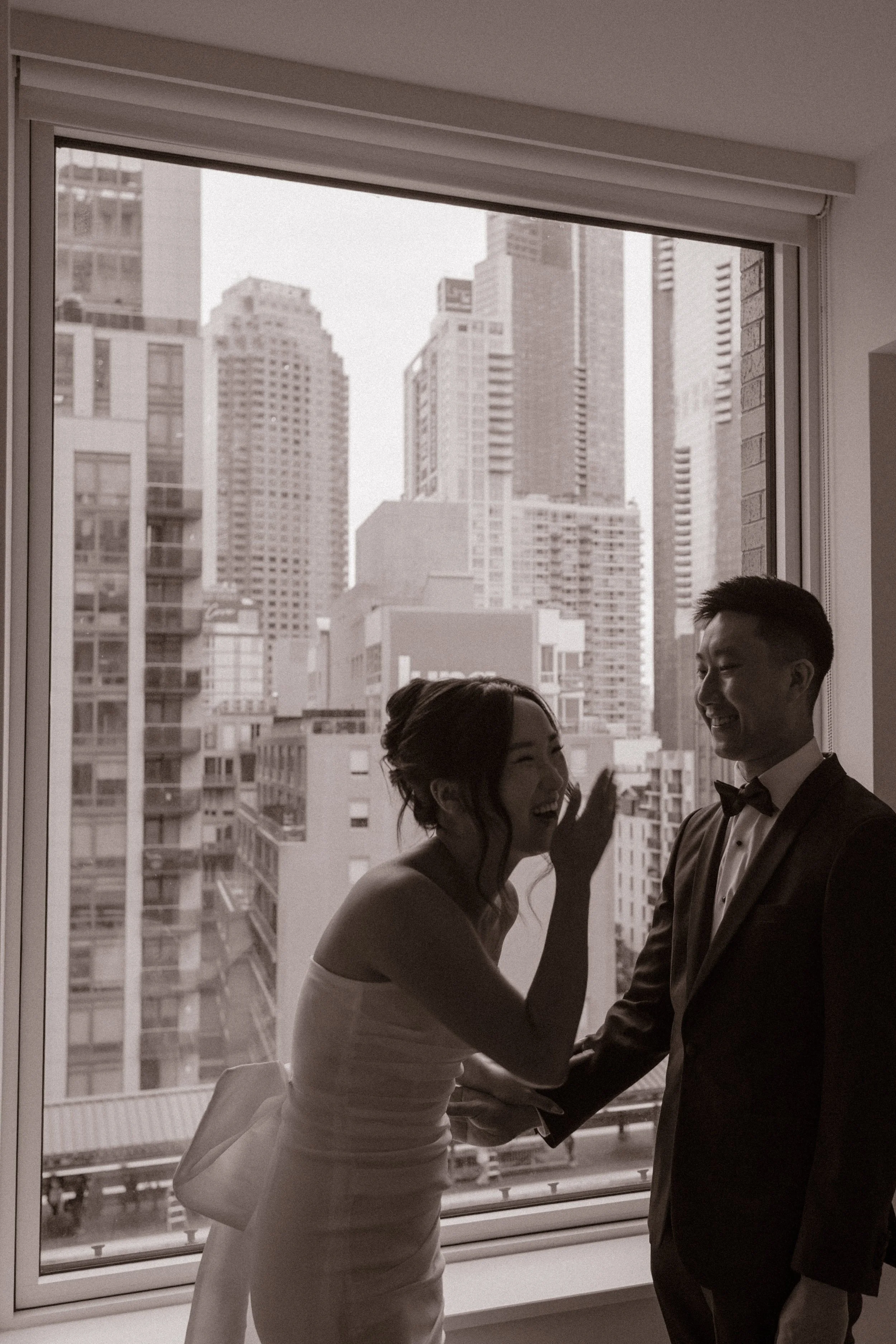 Bride laughing with the groom by their apartment window before leaving for their NYC courthouse wedding.