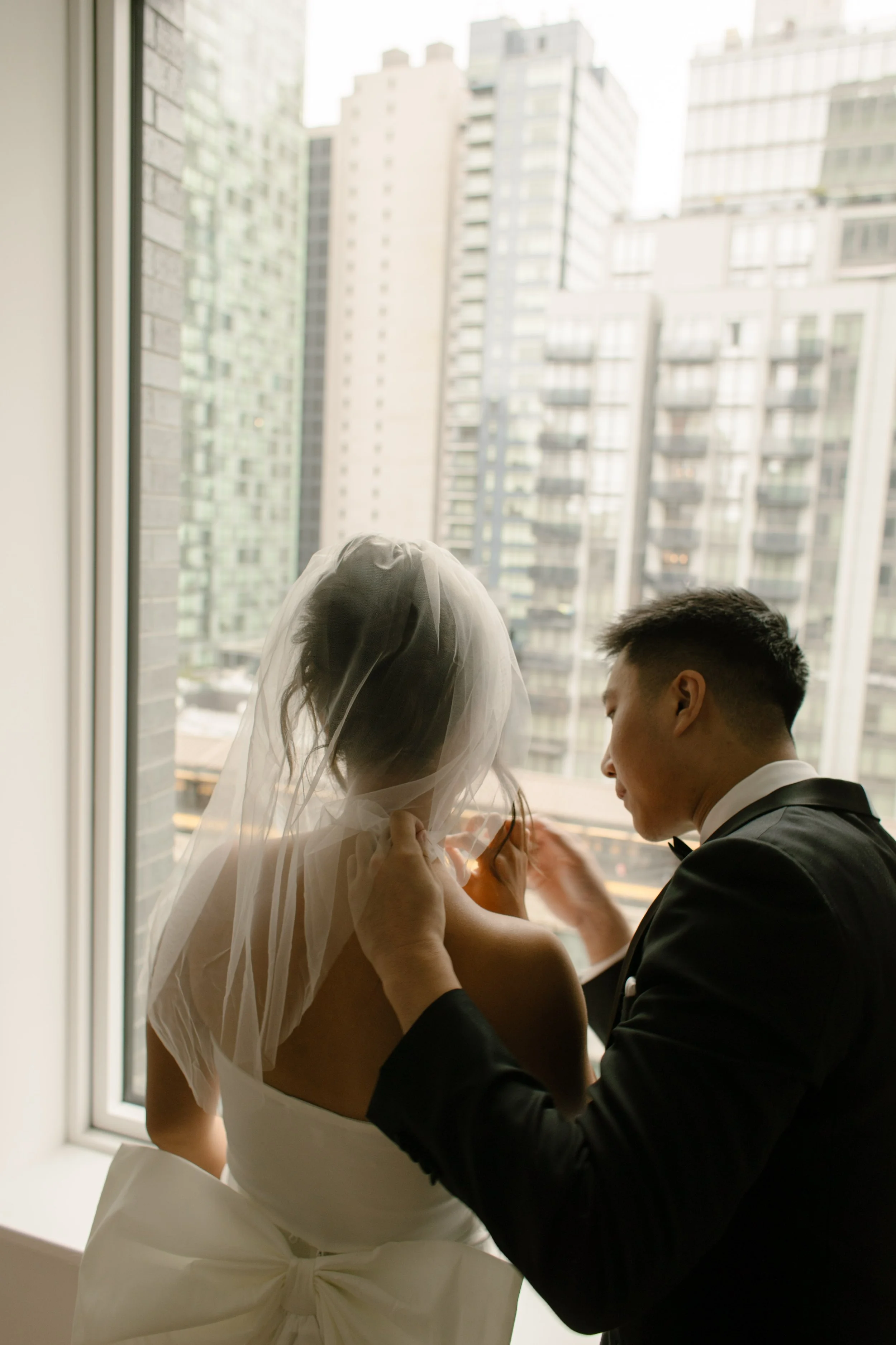 Groom fastening the bride's necklace while they get ready together in their apartment before their wedding day.