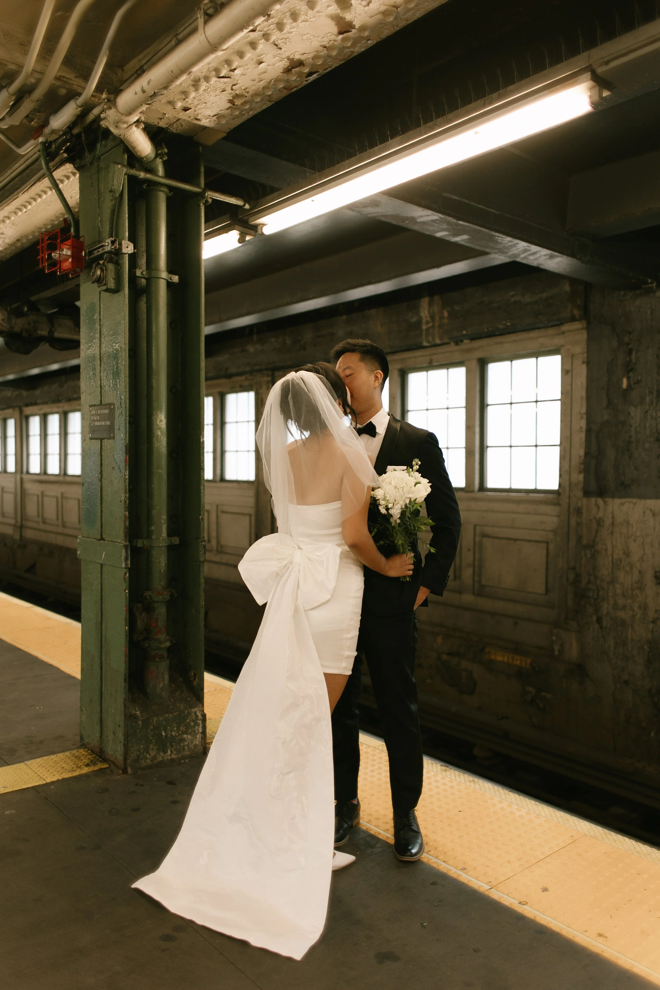 Bride and groom sharing a kiss on a New York City subway platform during their NYC courthouse wedding portraits.