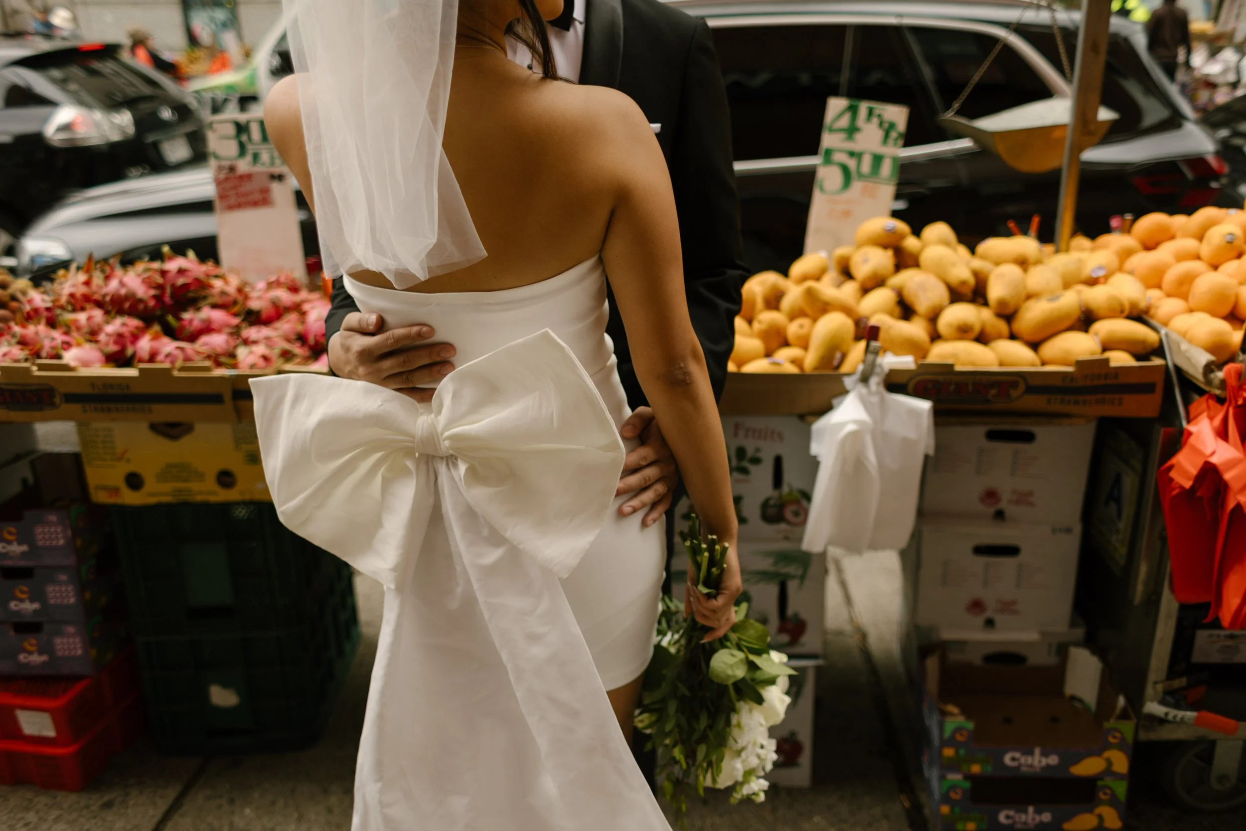 Close-up of the bride's oversized bow and bouquet as the couple embraces in a New York City street market.