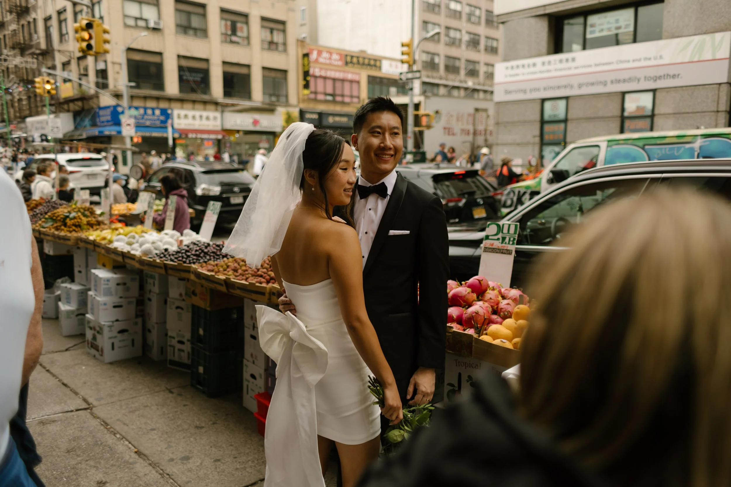 Bride and groom sharing a quiet portrait beside a bustling Chinatown fruit stand after their NYC courthouse wedding.