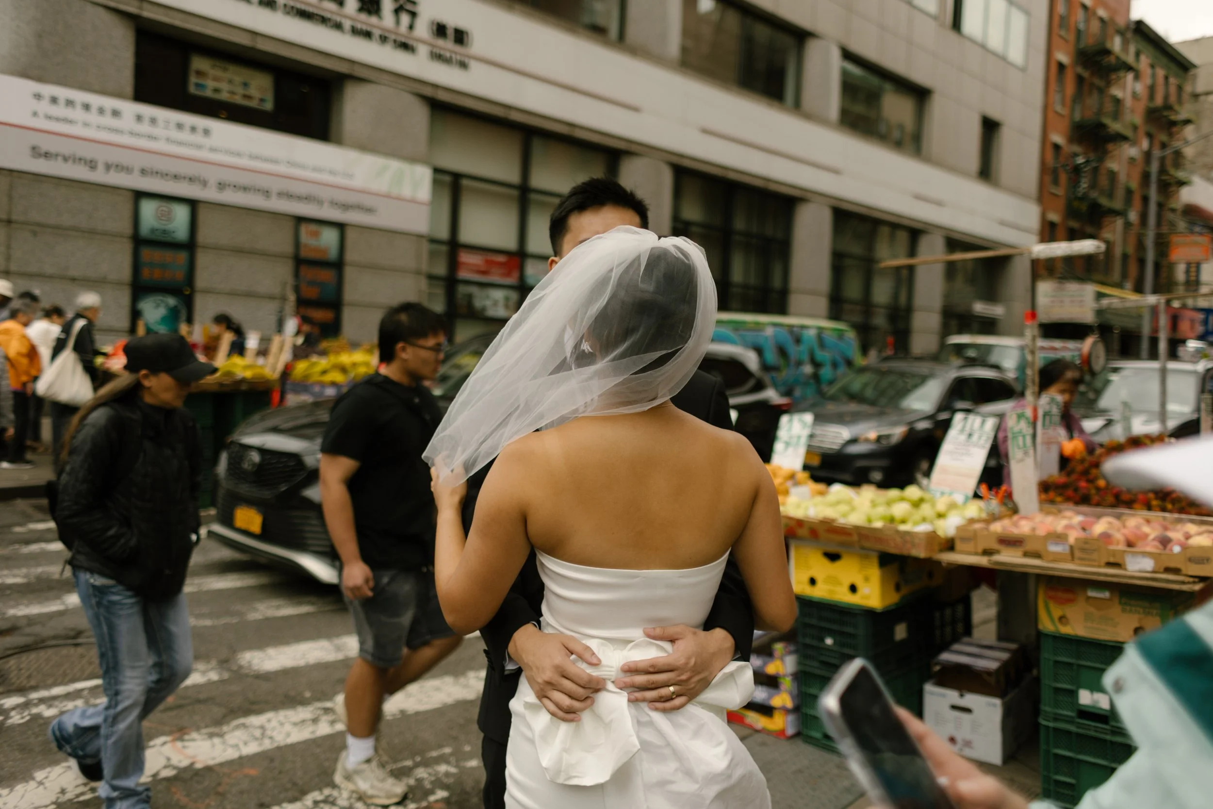 Bride and groom hug in the middle of a lively Manhattan neighborhood after their nyc courthouse wedding.