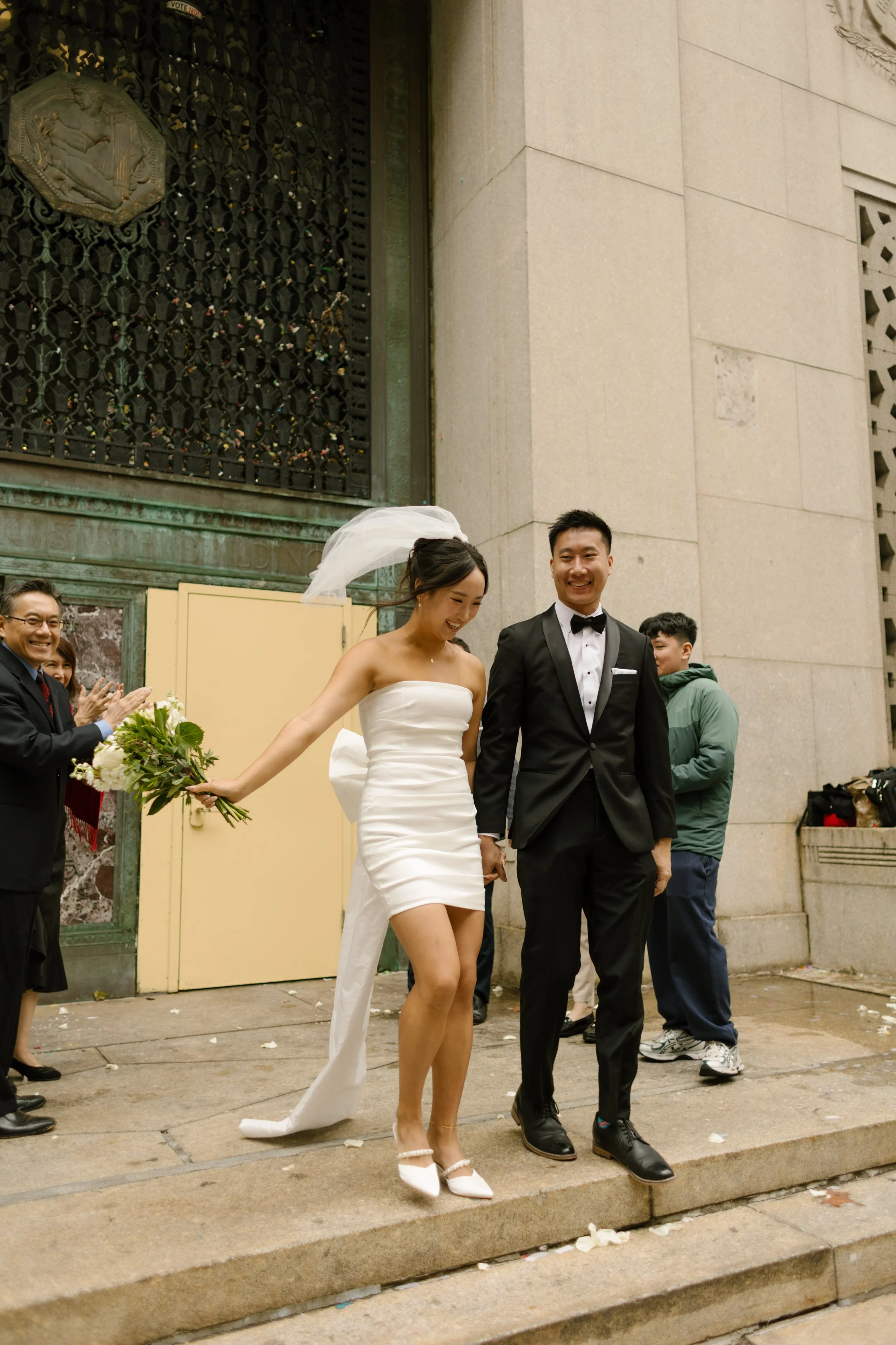 Joyful couple walks down the courthouse steps after their nyc courthouse wedding while guests applaud.