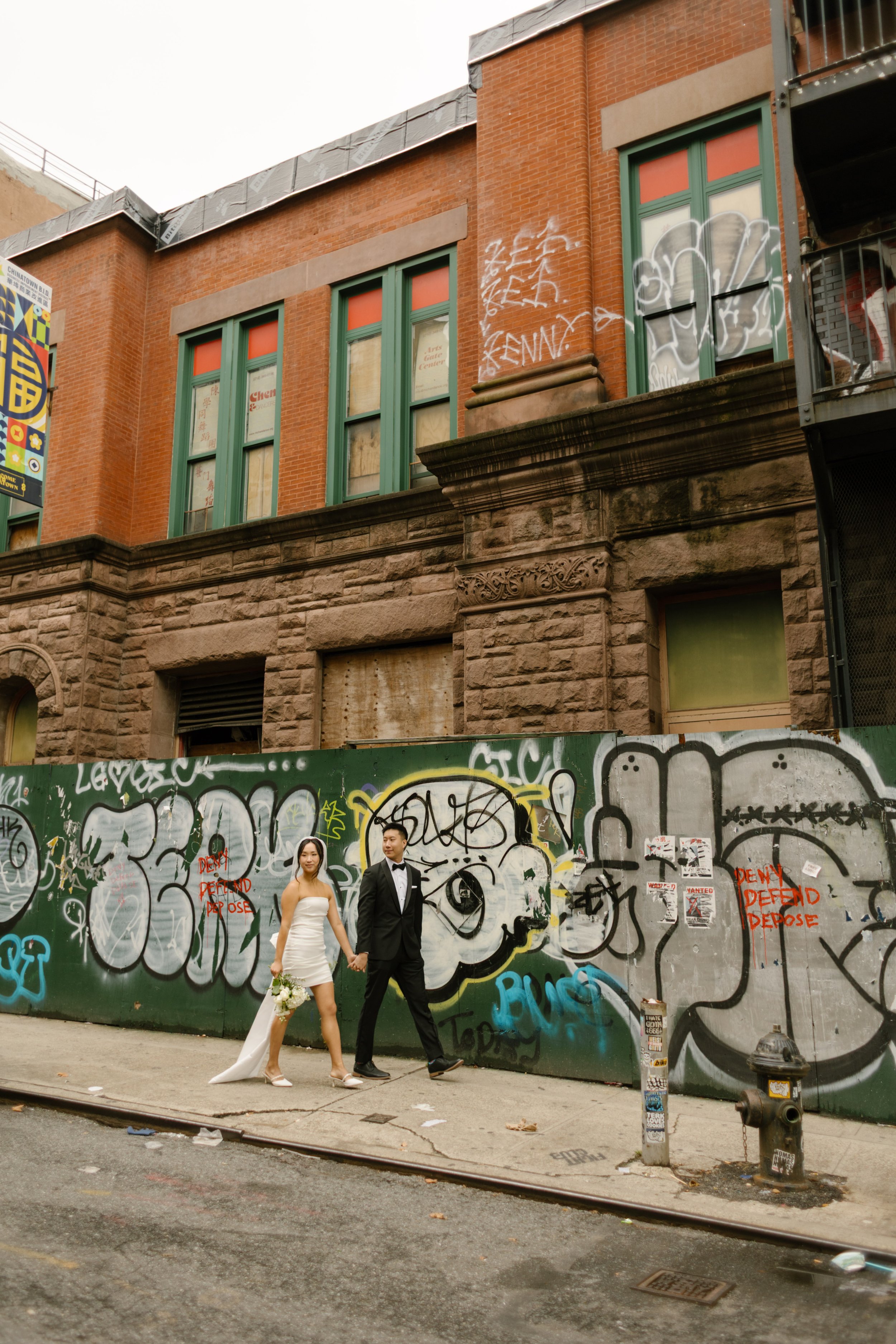 Newlyweds walk hand in hand past colorful graffiti murals after their nyc courthouse wedding.