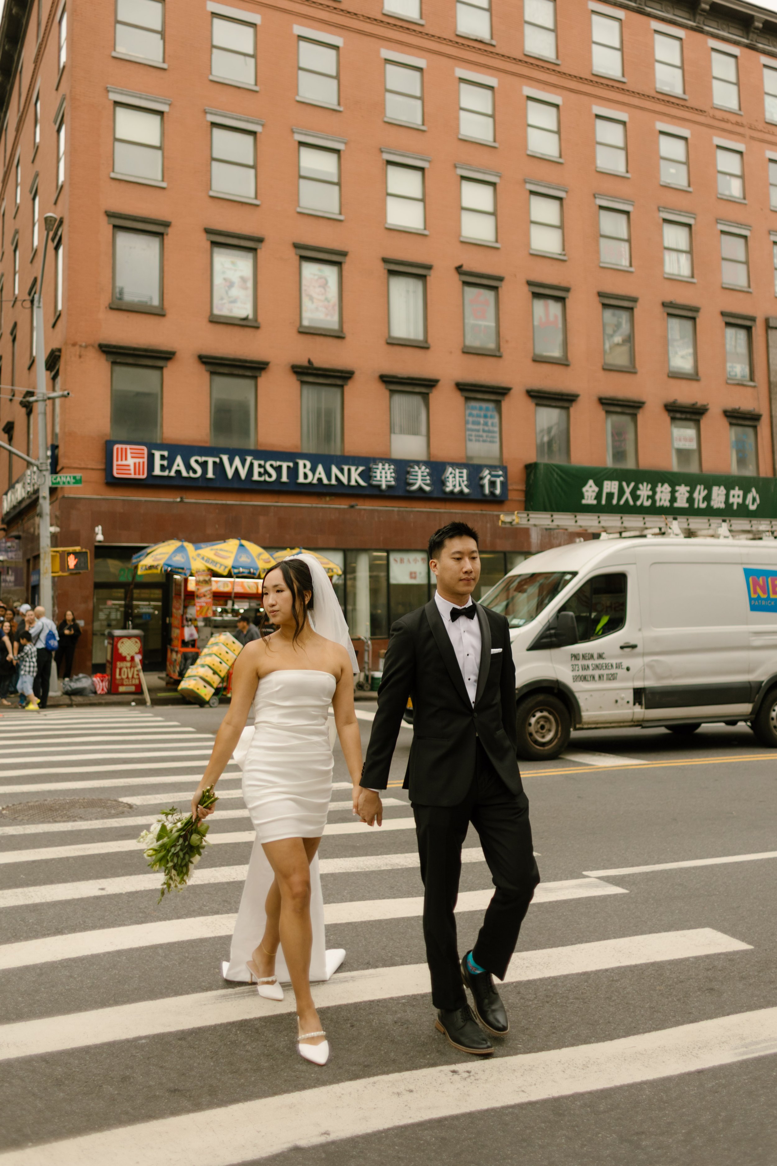 Couple crosses a Chinatown crosswalk hand in hand after their nyc courthouse wedding.