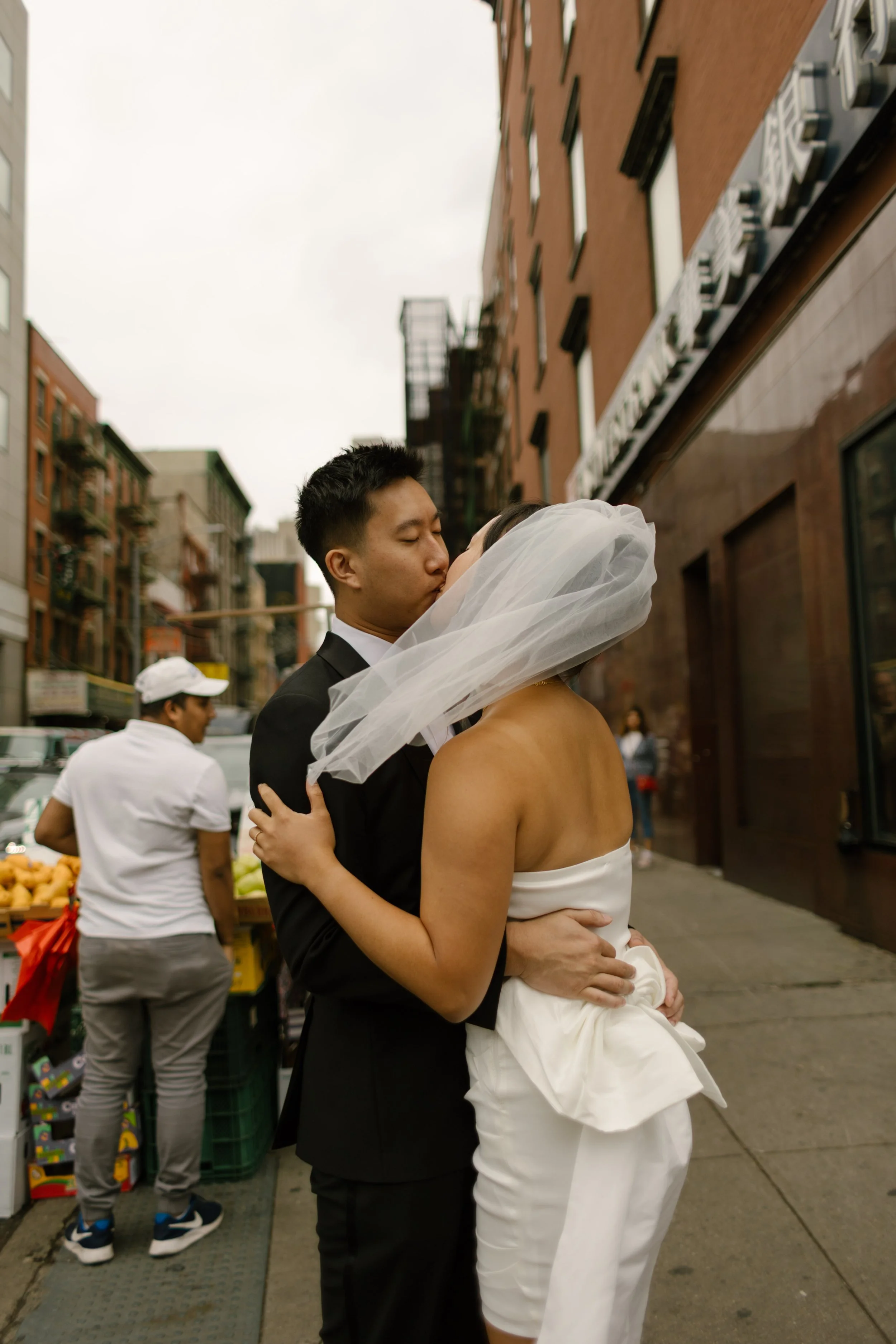 Bride and groom share a kiss on a bustling Lower Manhattan sidewalk after their intimate wedding ceremony.
