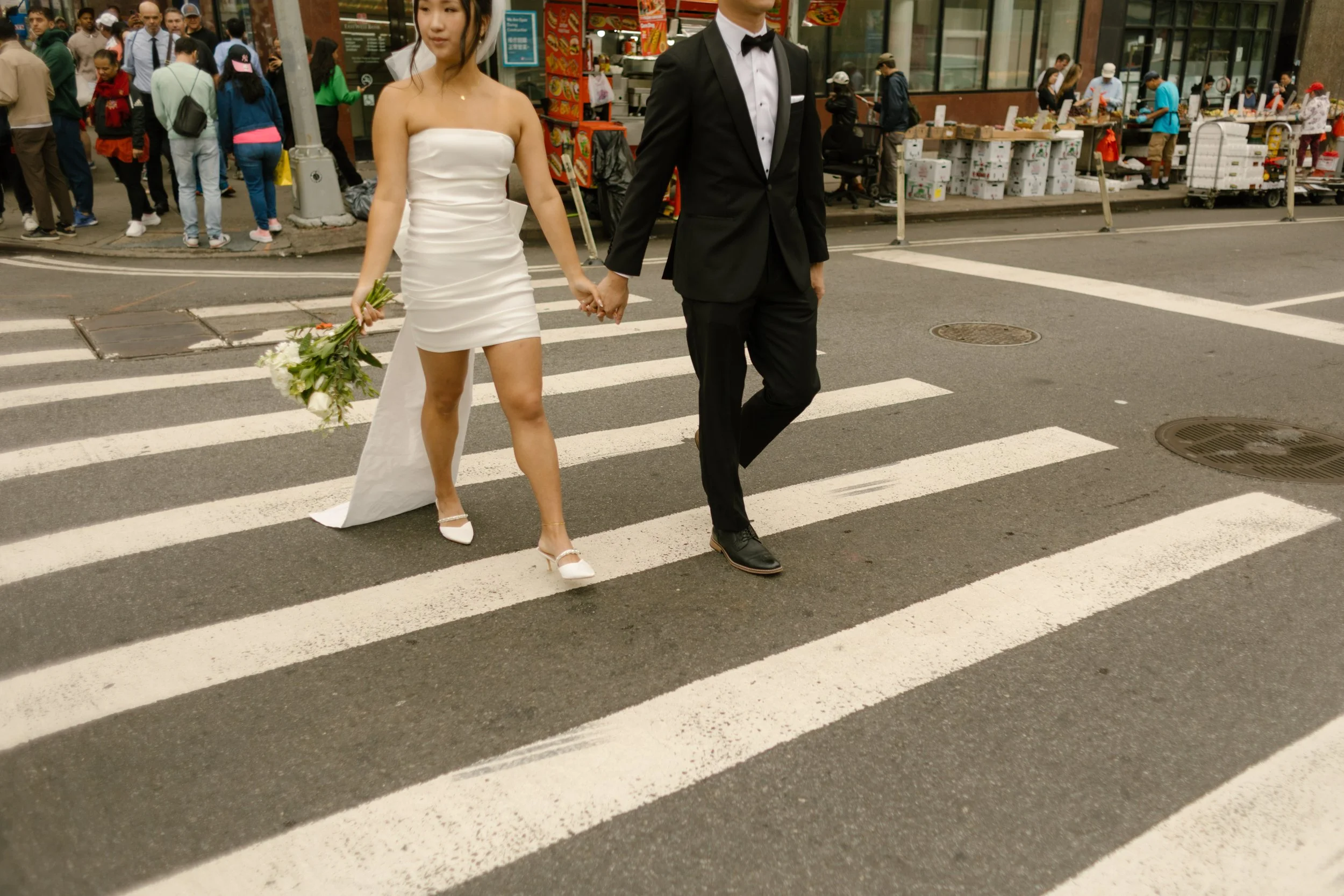 Bride and groom hold hands while crossing a Manhattan crosswalk after their intimate courthouse ceremony.