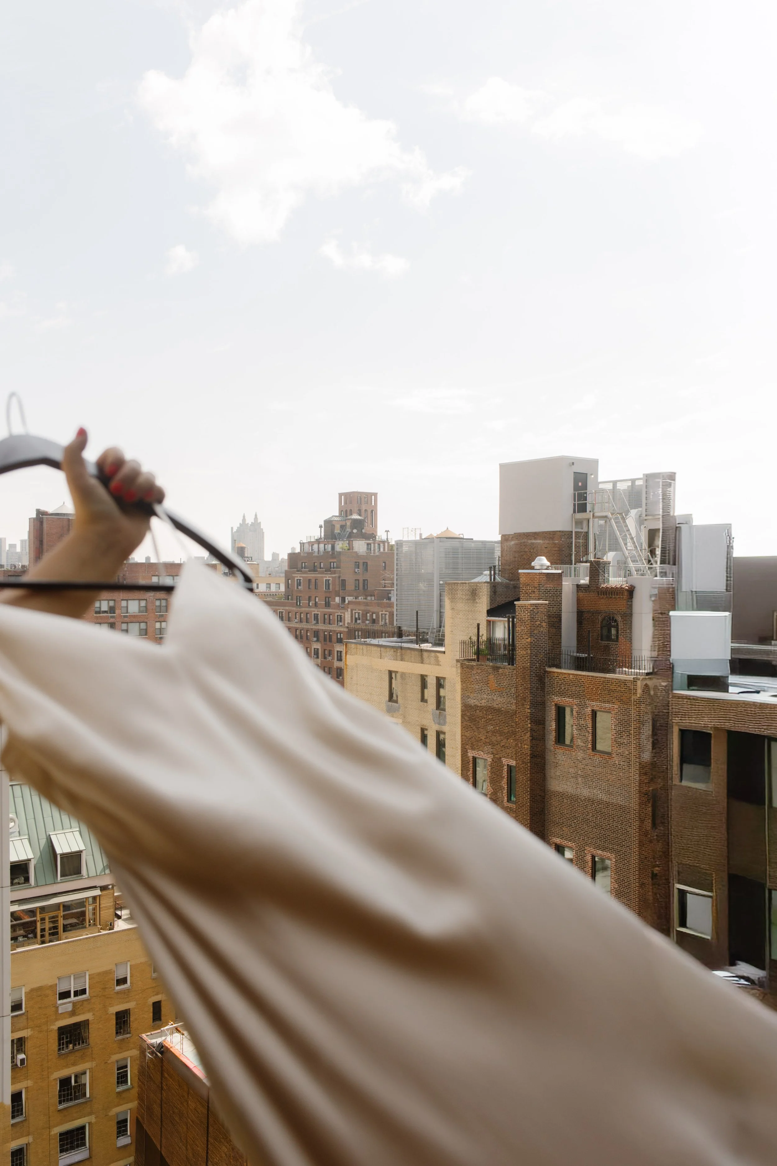 Wedding dress held up in front of a hotel window with the New York City skyline in the background as part of the wedding day timeline.