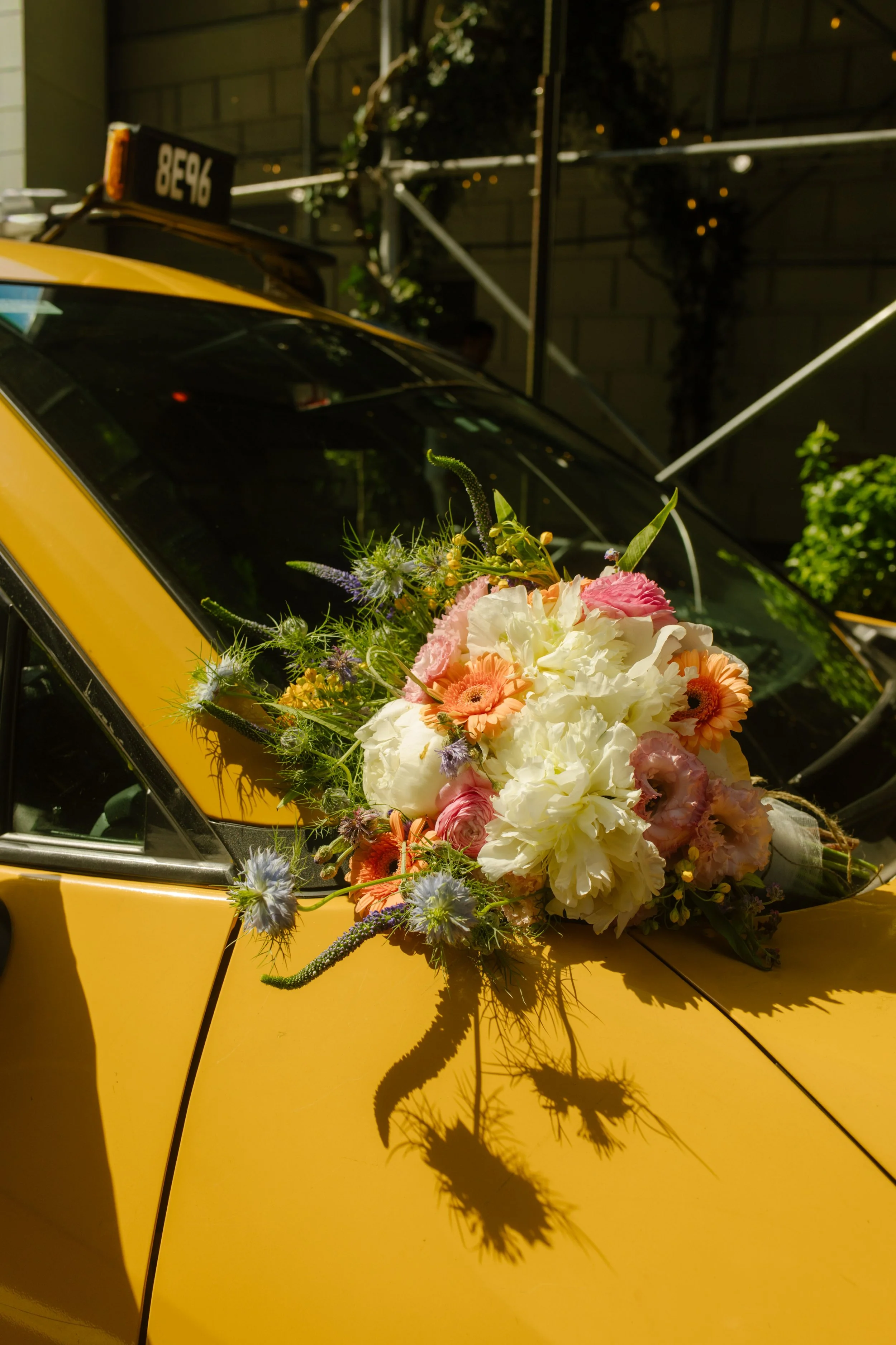 Colorful bridal bouquet resting on the hood of a classic yellow New York City taxi.