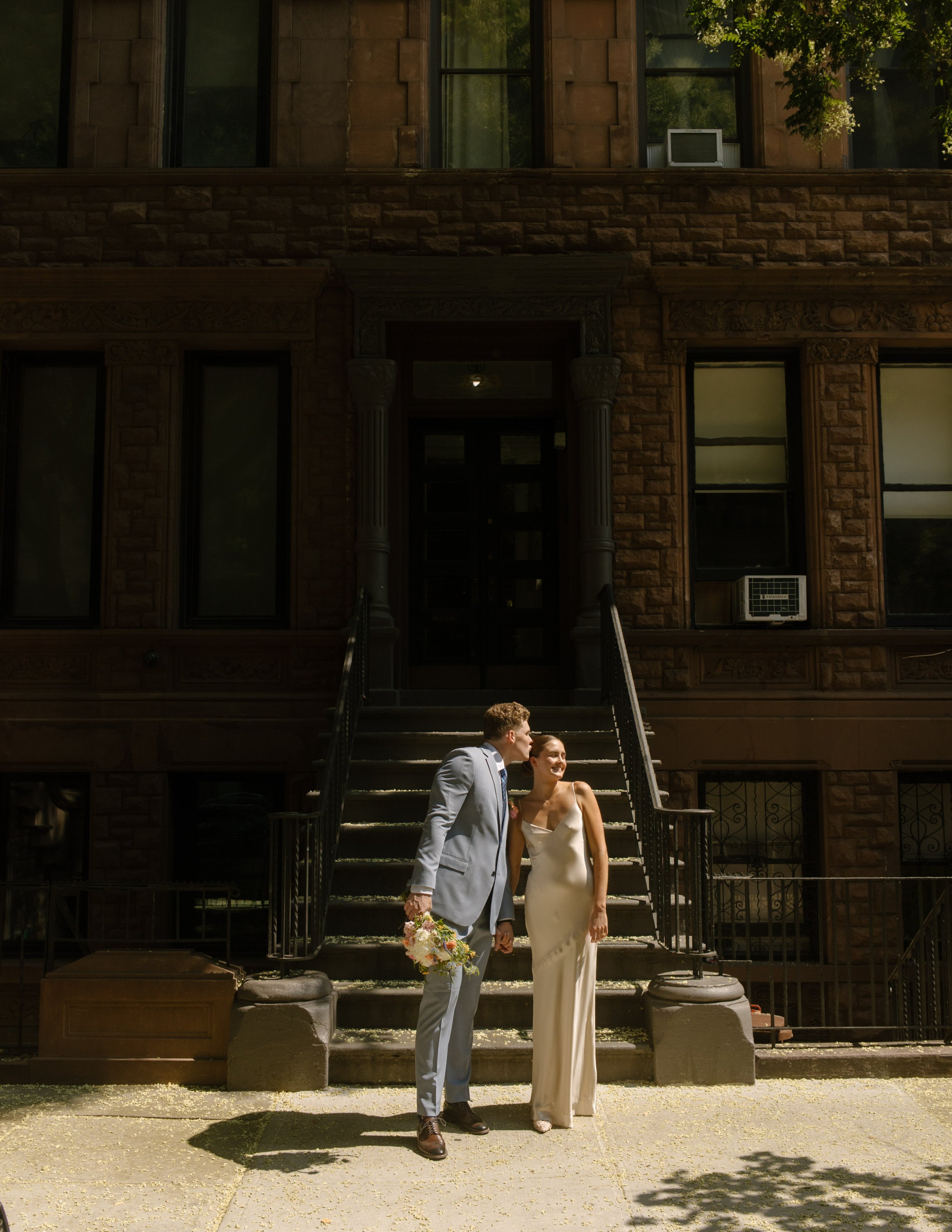 Bride and groom sharing a kiss outside a brownstone on their wedding day timeline portrait stop.