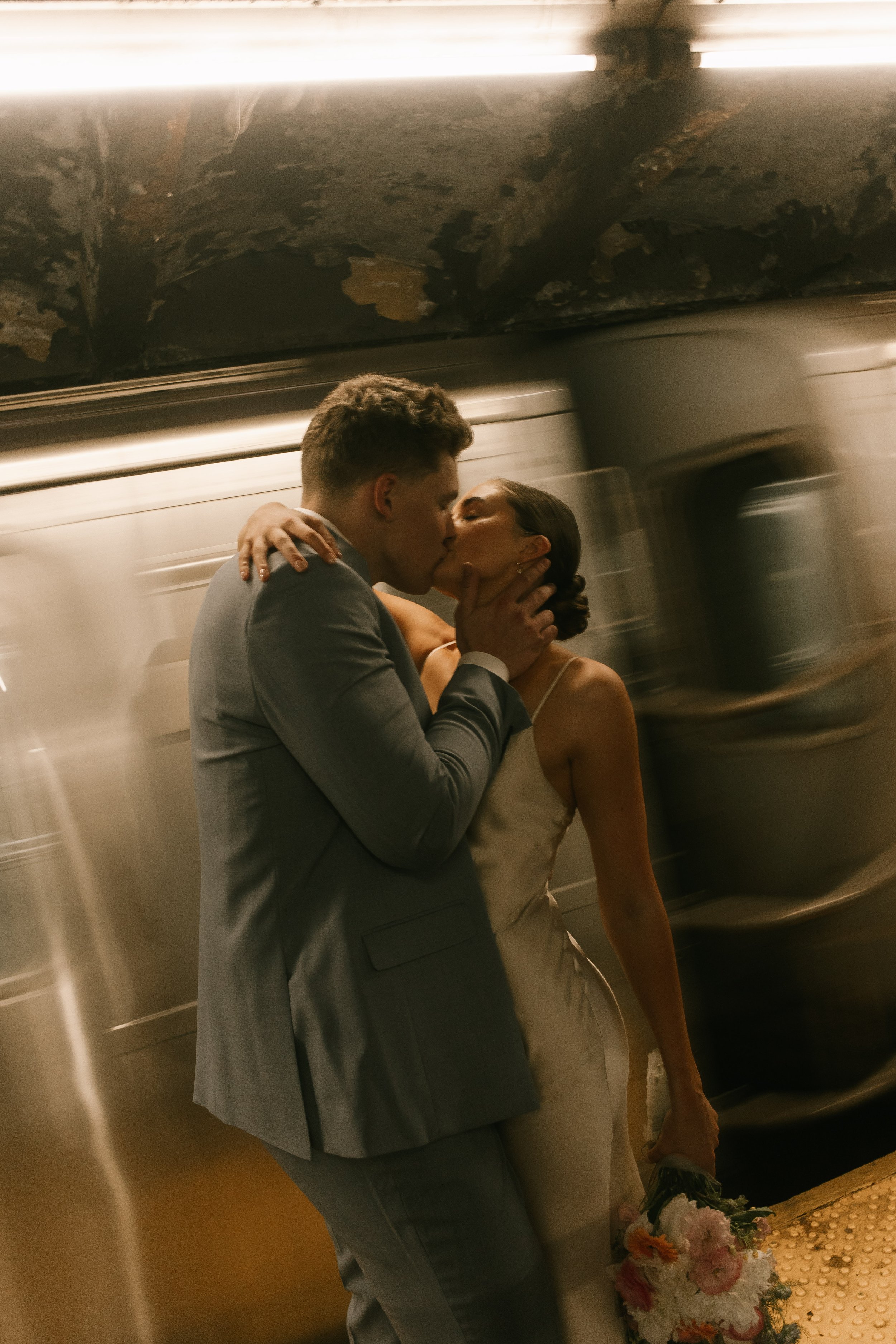 Bride and groom sharing a kiss on a moving New York City subway platform after their ceremony.