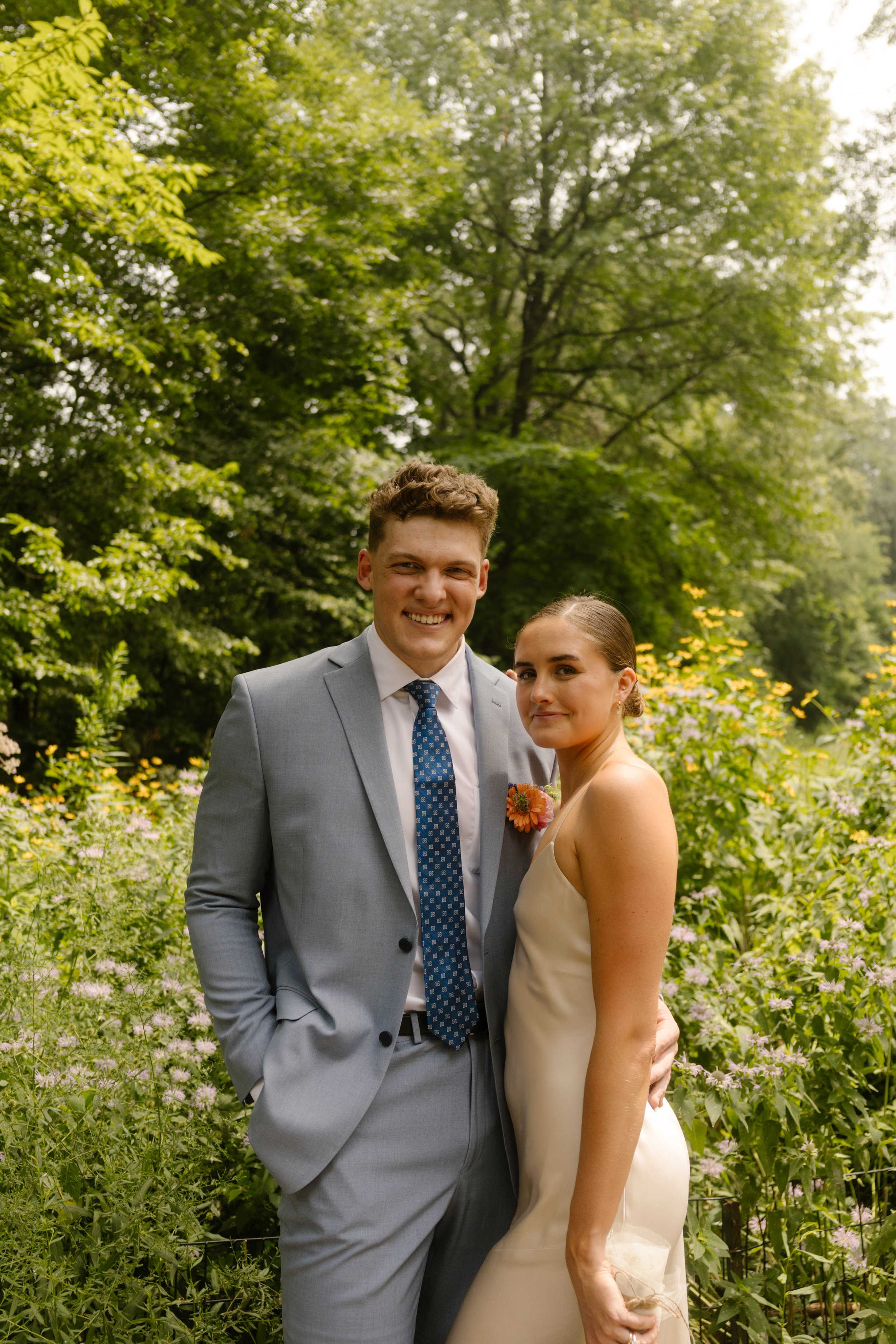 Newly married couple posing together in a lush city garden during their wedding day timeline portraits.