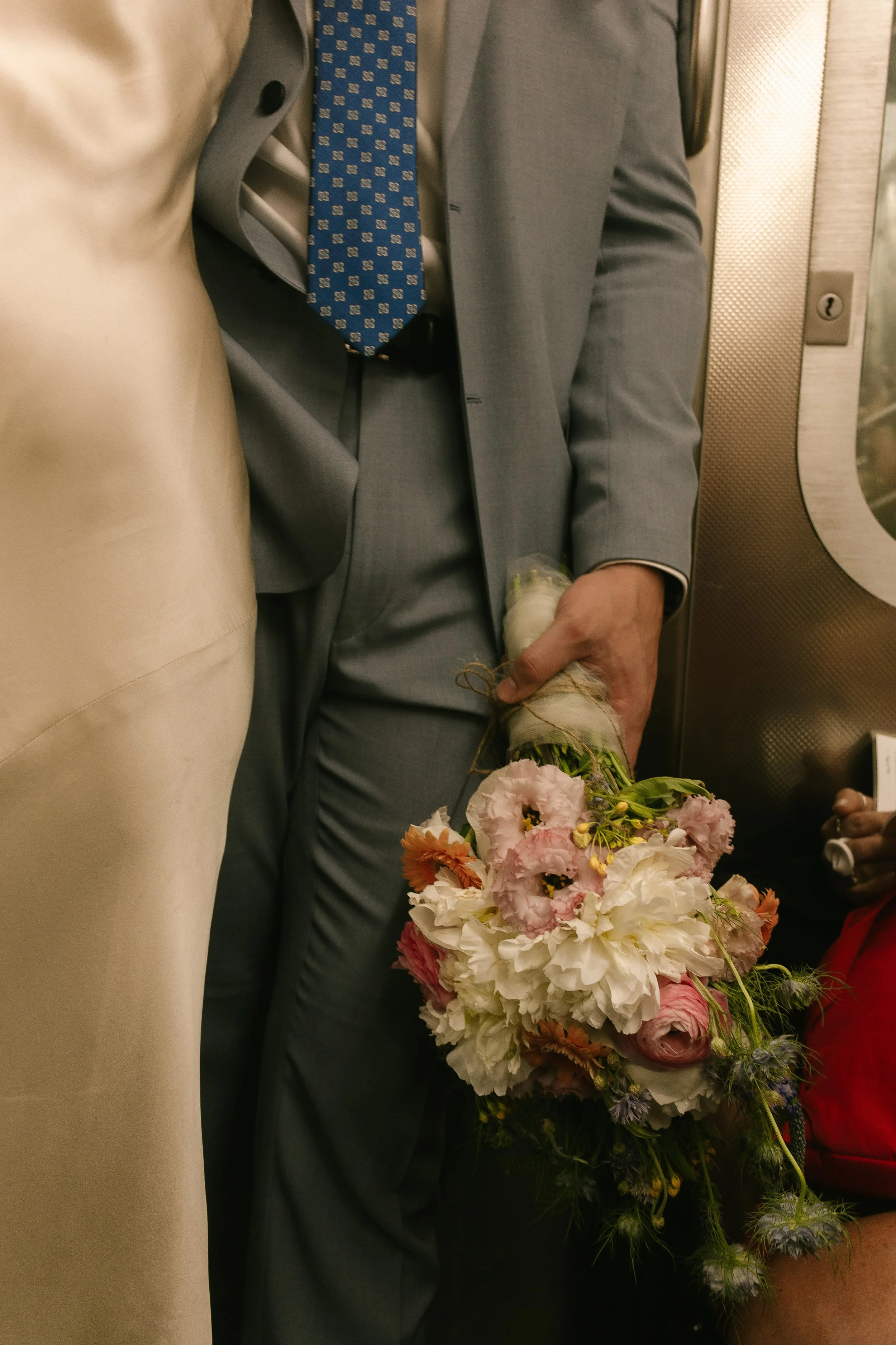 Groom holding the bride's bouquet while riding the subway after the ceremony.