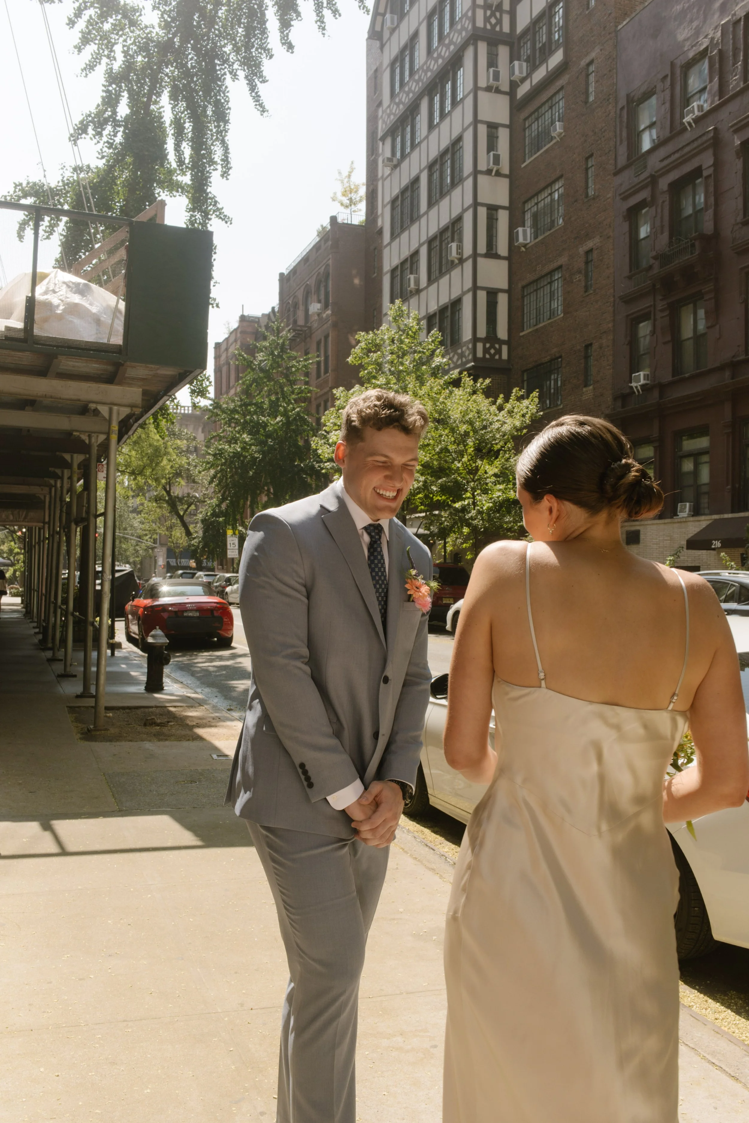 Bride and groom smiling at each other during their first look on a New York City sidewalk.