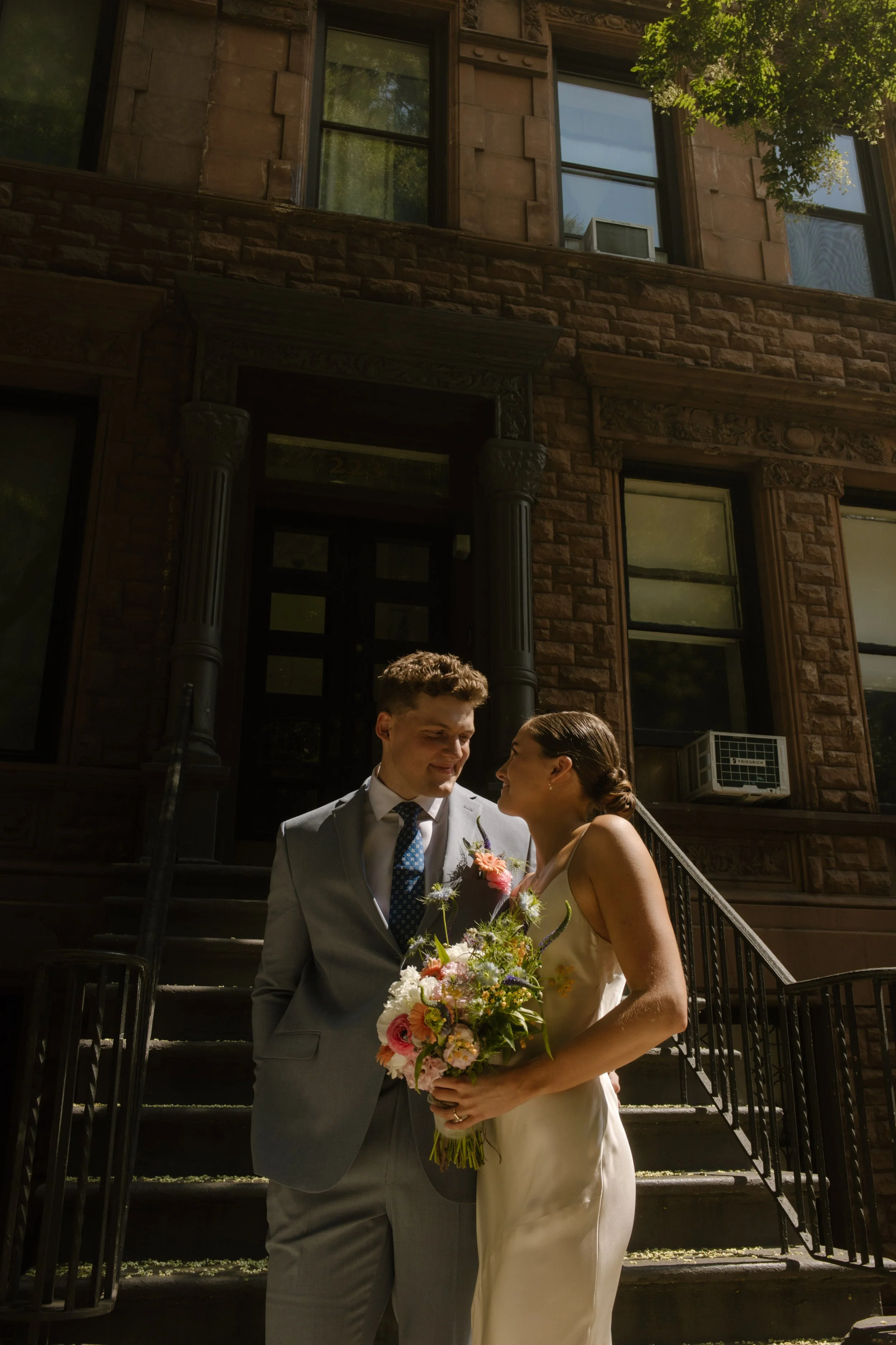 Bride and groom smiling at each other outside a brownstone during their wedding day timeline portraits.