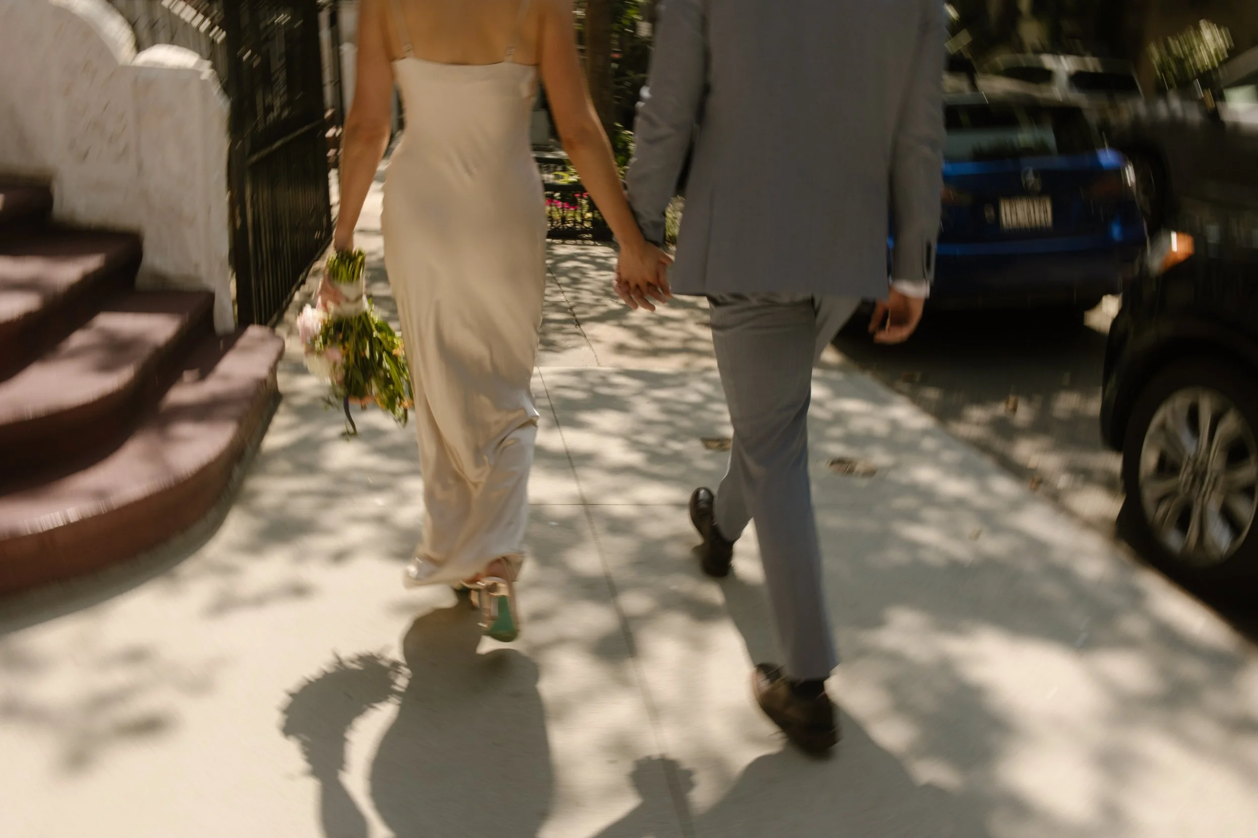 Bride and groom holding hands while walking through a tree-lined New York street during their wedding day timeline.