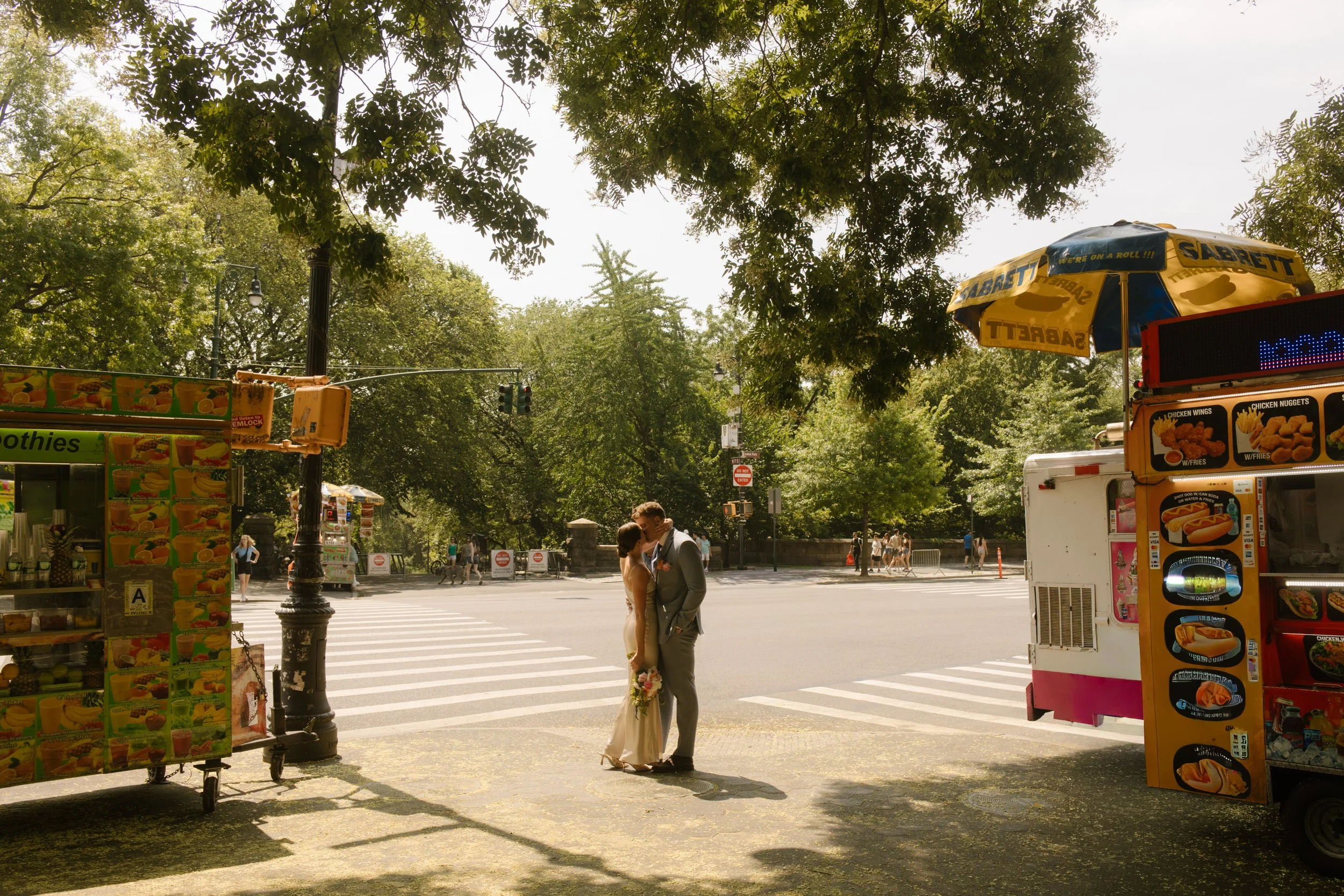 Couple sharing a kiss at a crosswalk near Central Park surrounded by iconic New York City streets.