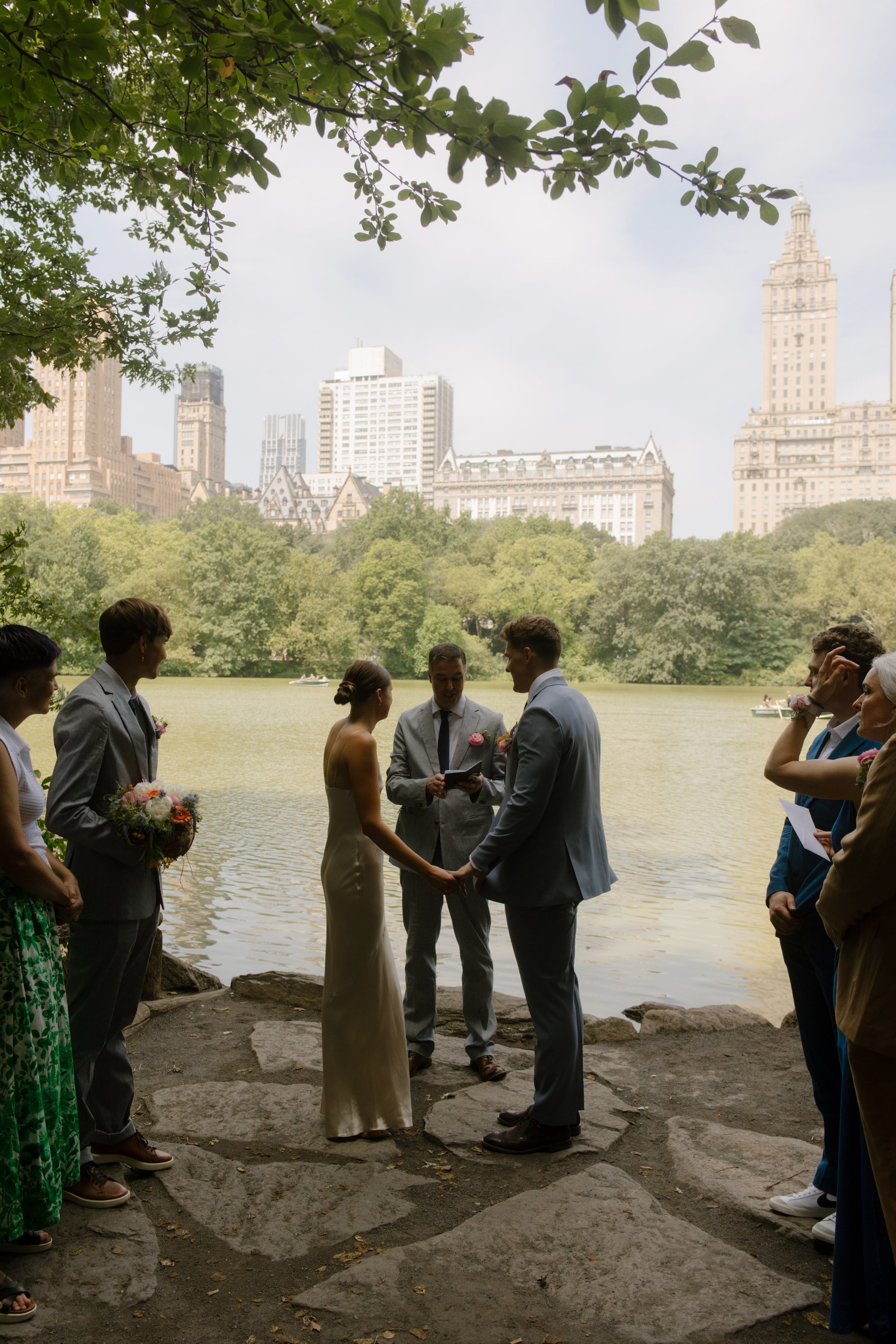 Intimate lakeside wedding ceremony in Central Park with the New York City skyline in the background as part of the wedding day timeline.