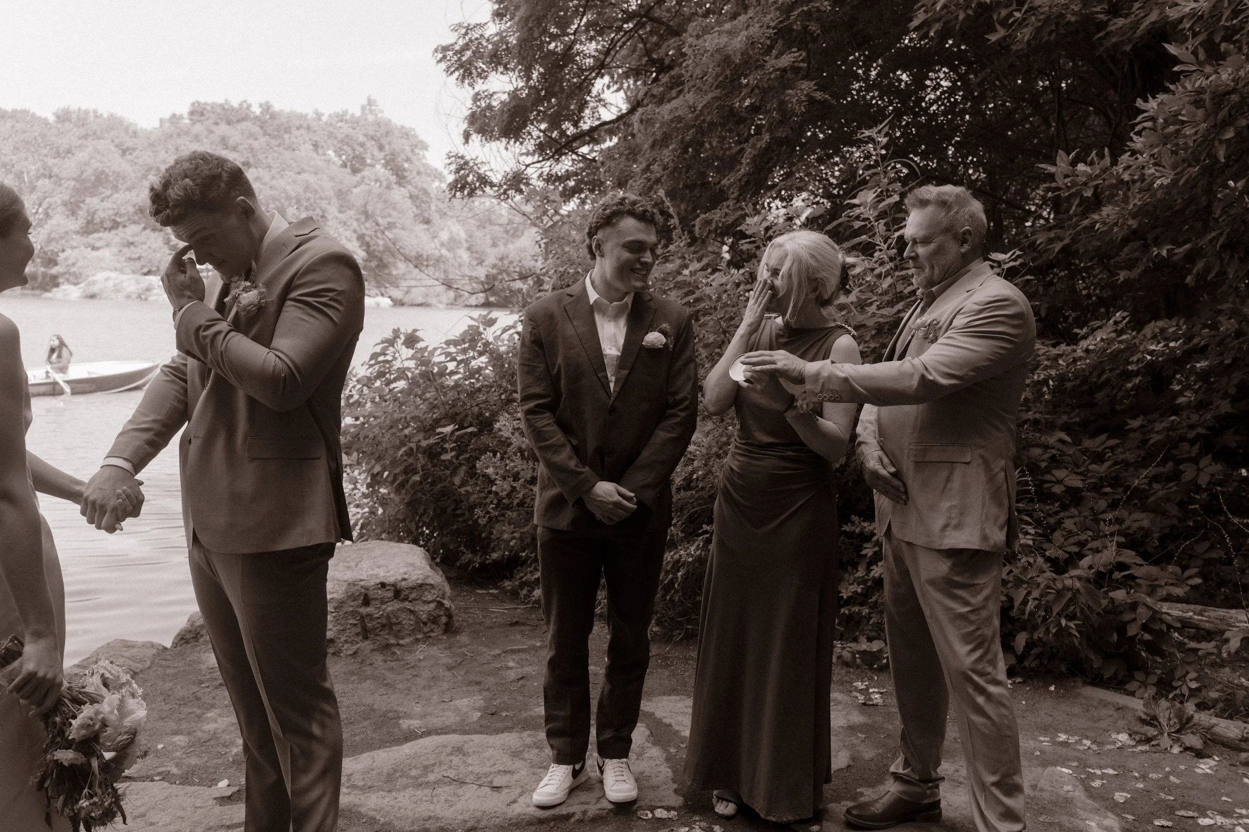 Emotional family members embracing during the ceremony while the groom wipes away tears.