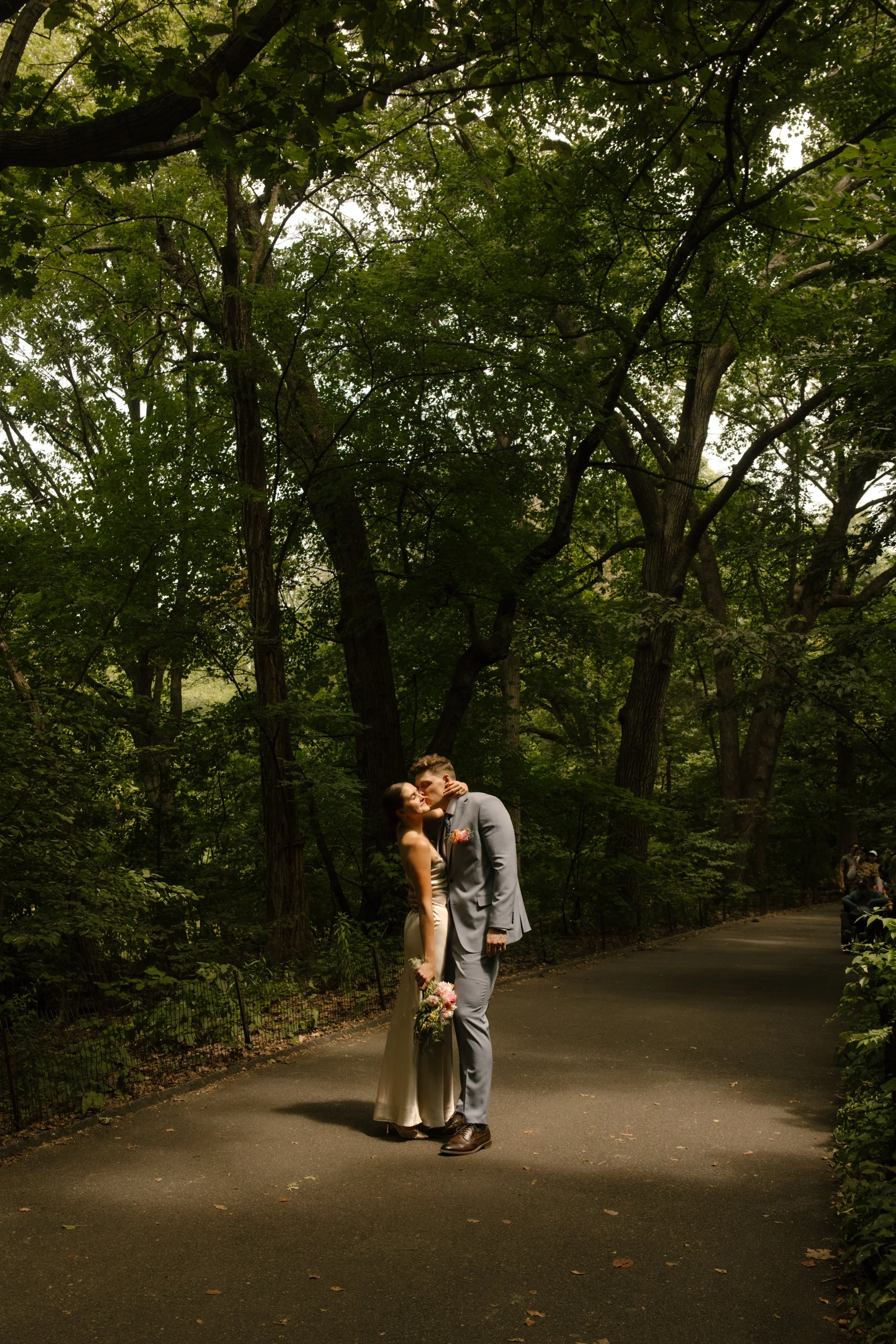 Newlyweds sharing a quiet kiss on a shaded Central Park pathway after the ceremony.