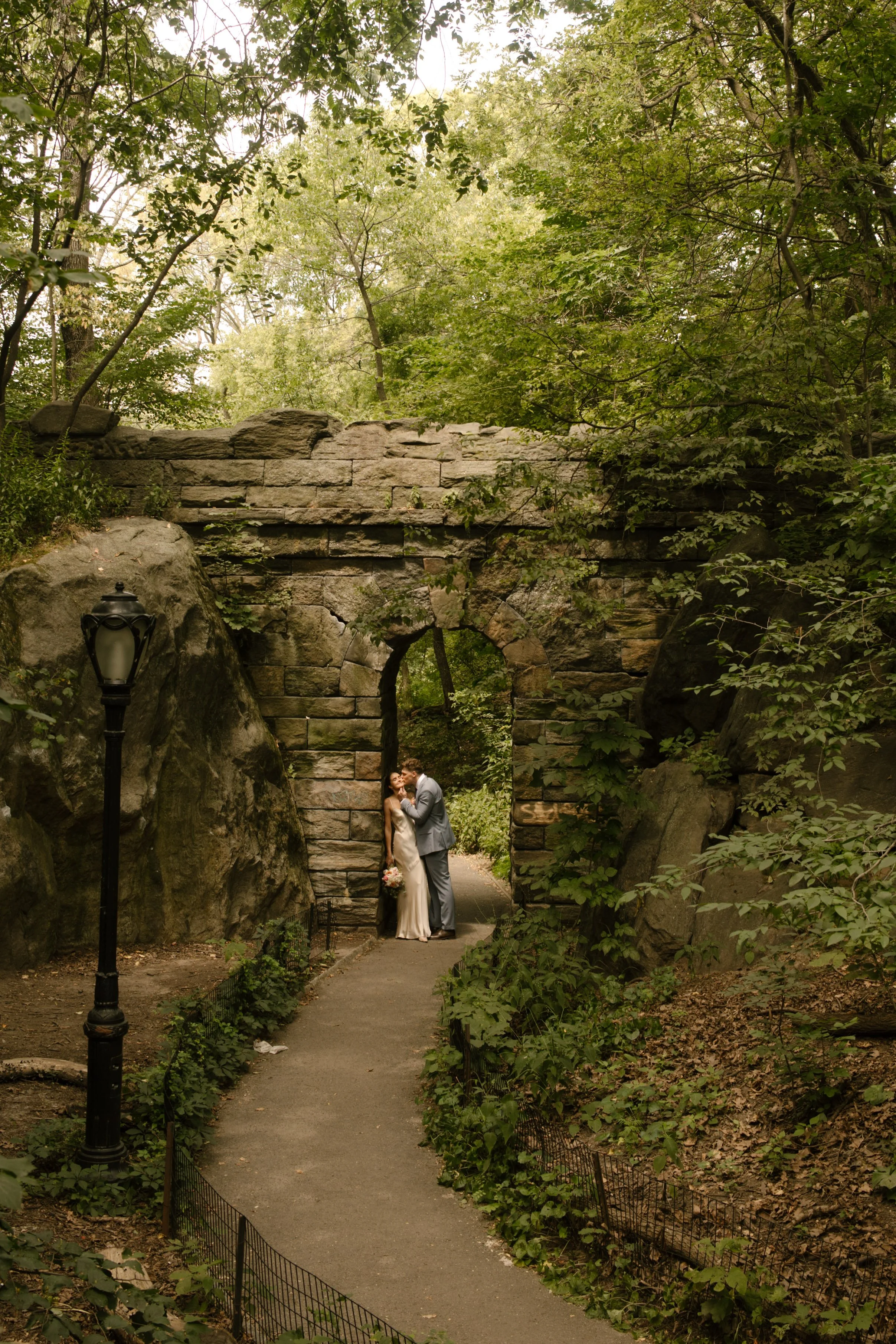 Bride and groom standing beneath a stone arch in Central Park after their ceremony.