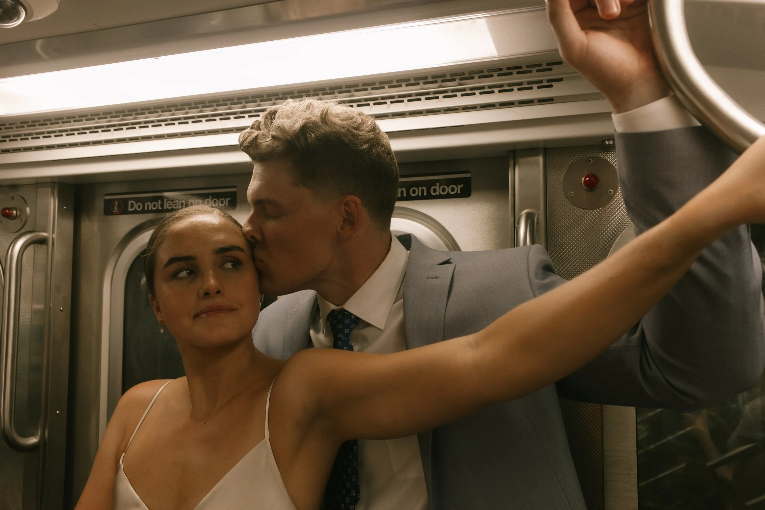 Groom kissing the bride's forehead while riding a New York City subway during their wedding day timeline portraits.