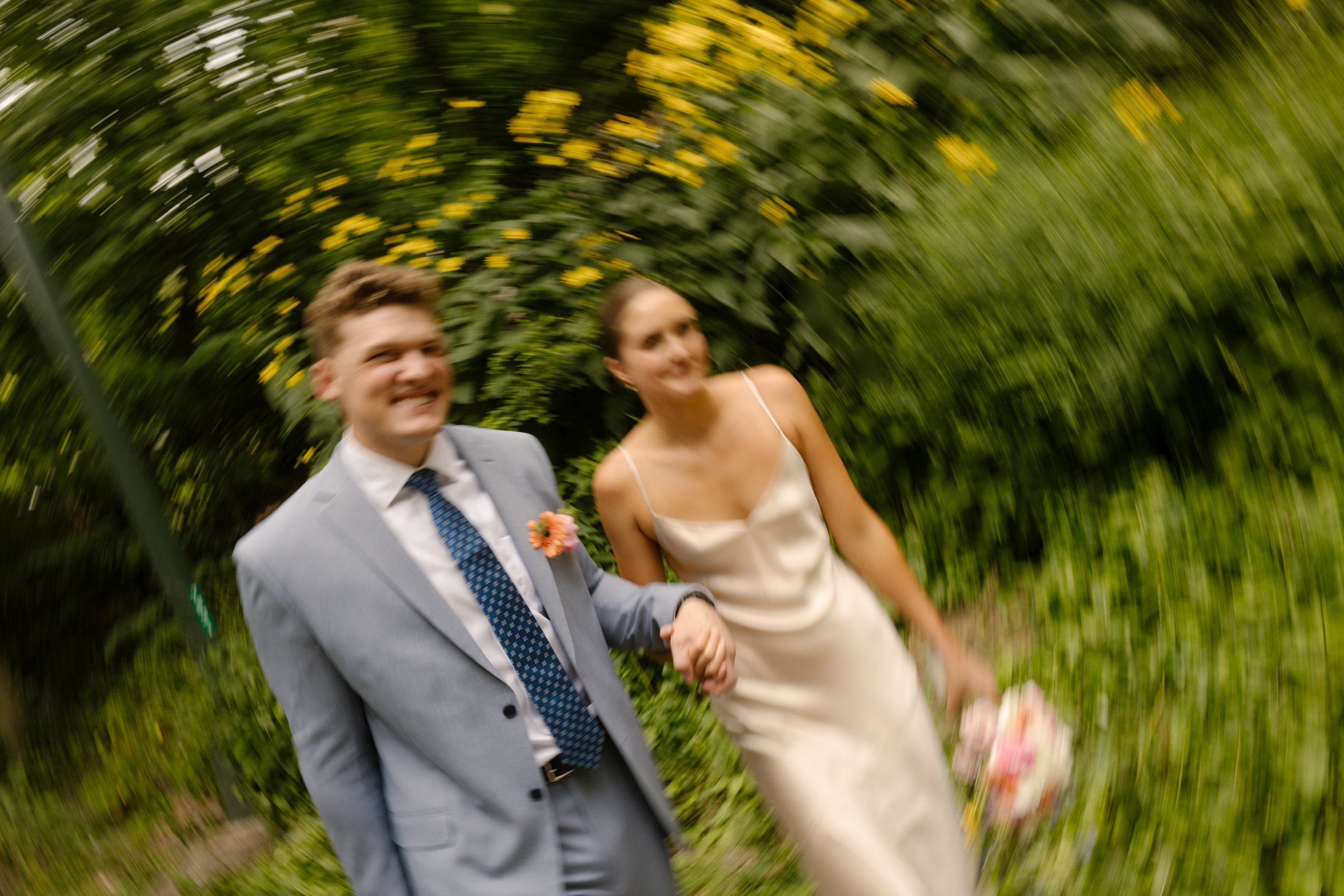 Motion blur portrait of the newlyweds walking together through a garden, adding a playful moment to their wedding day timeline.