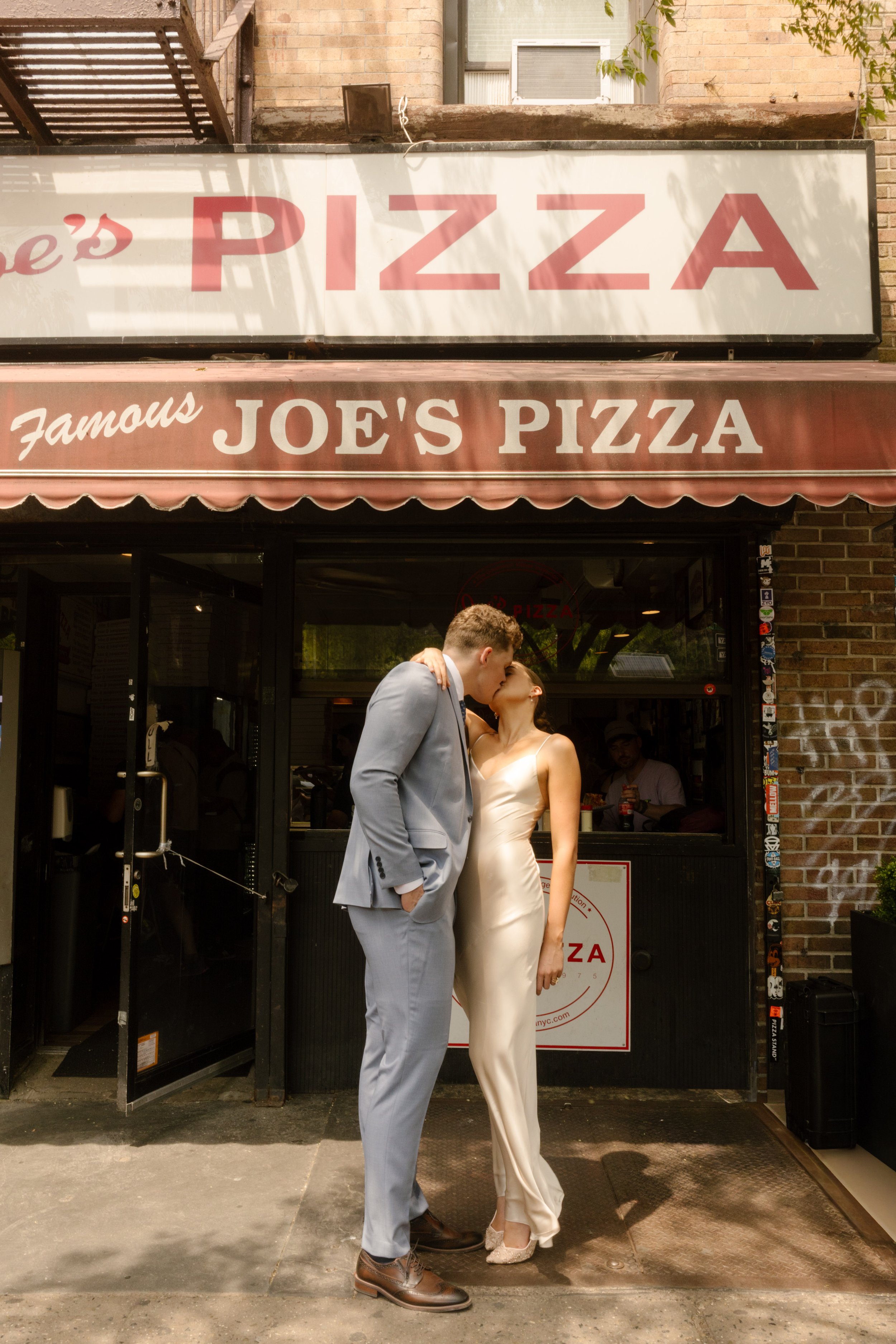 Bride and groom sharing a kiss outside Joe's Pizza during a classic New York wedding portrait stop.