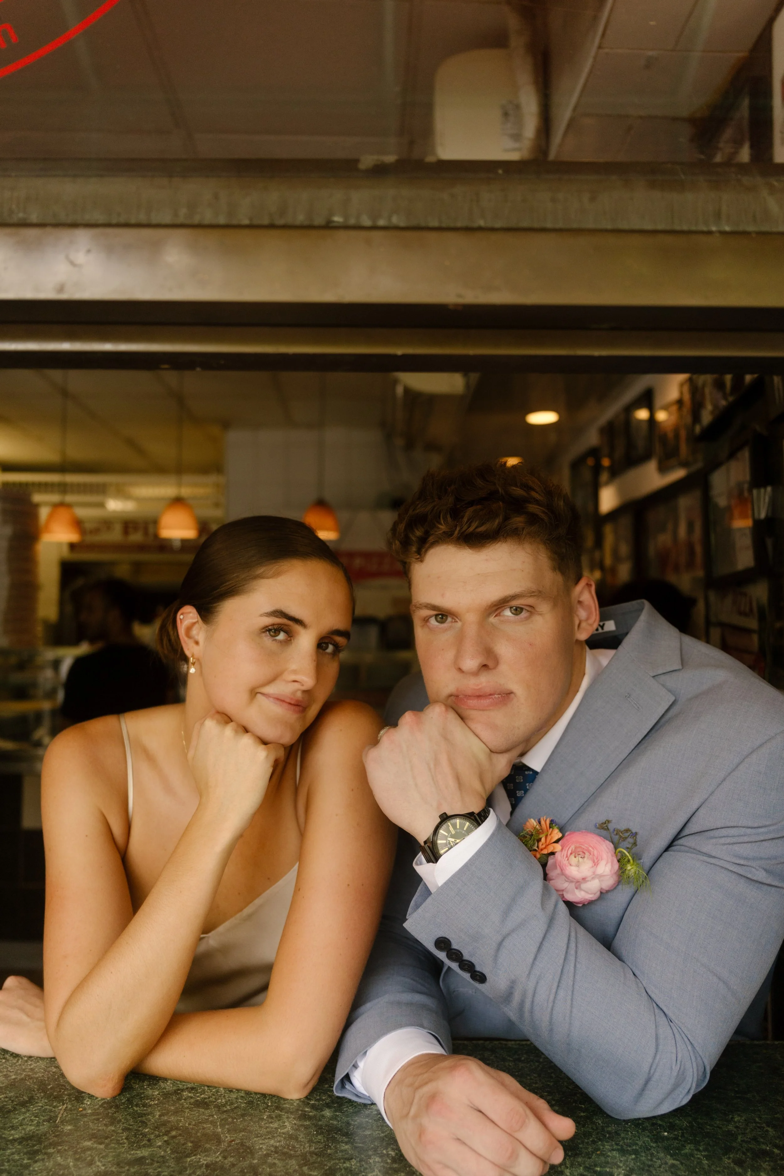 Newlyweds posing together inside a New York pizza shop during a relaxed break in their wedding day timeline.