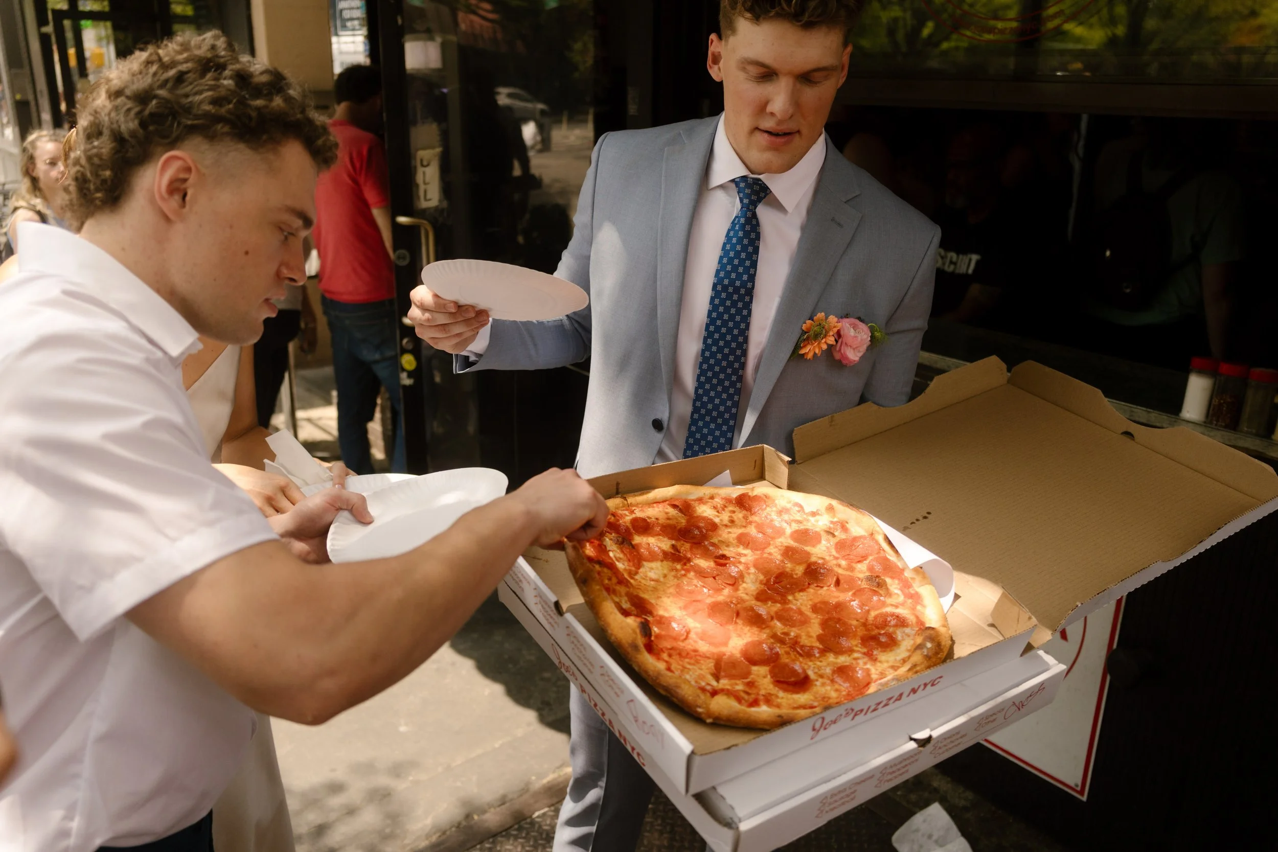 Wedding guests serving themselves slices of New York pizza during a casual reception meal in the wedding day timeline.