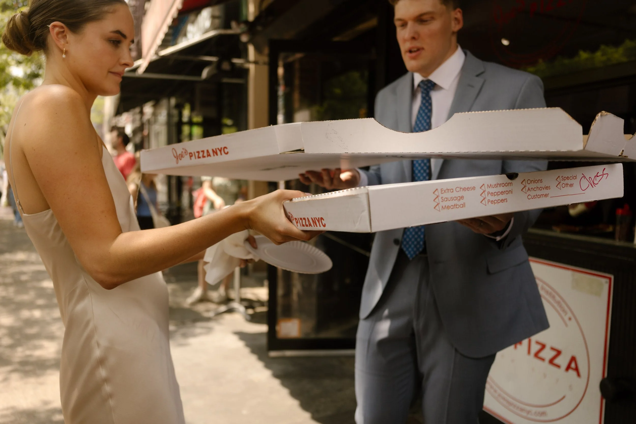 Bride carrying pizza boxes outside a New York pizzeria after the ceremony.