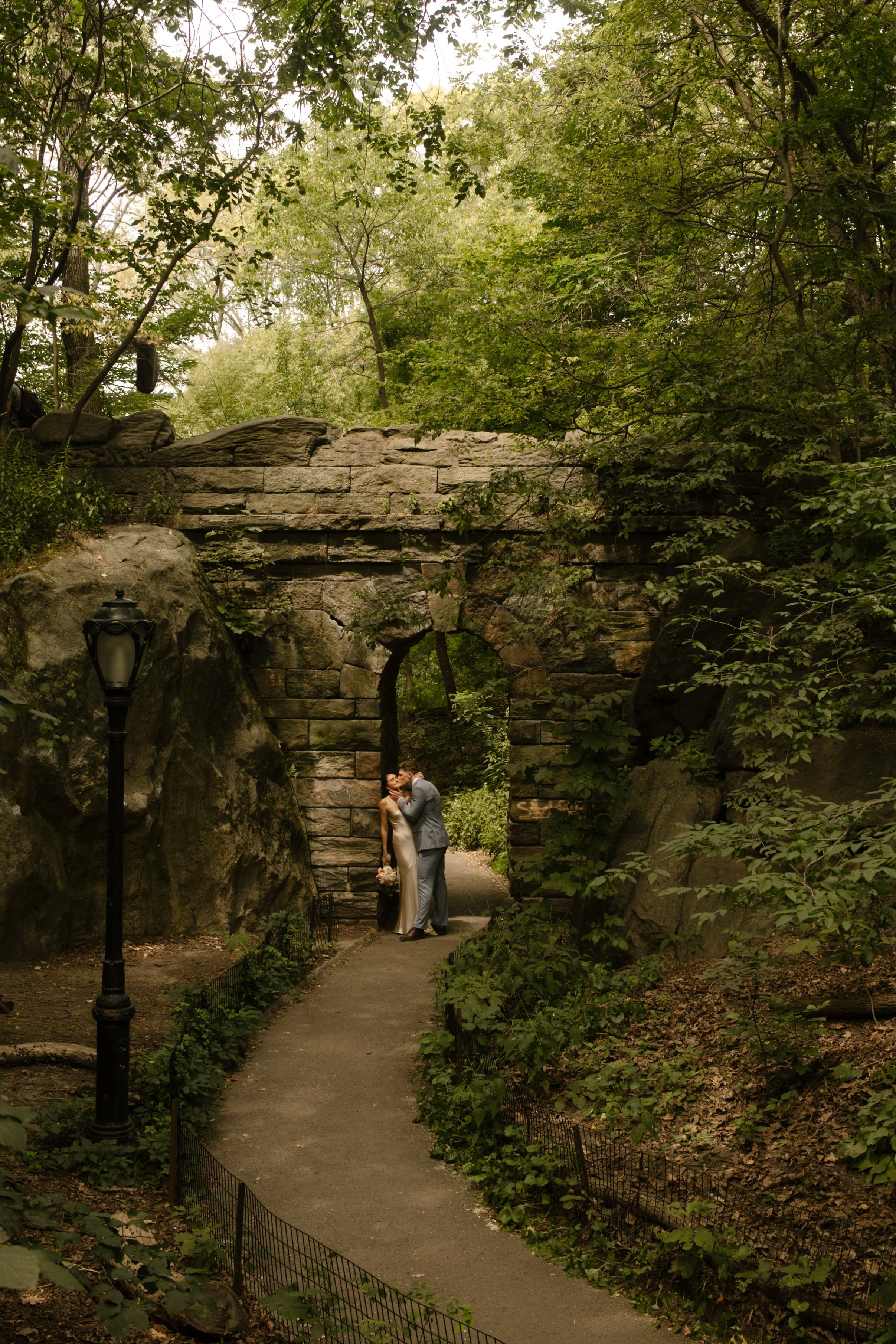 Wide portrait of the bride and groom beneath the iconic stone arch in Central Park during their wedding day timeline.