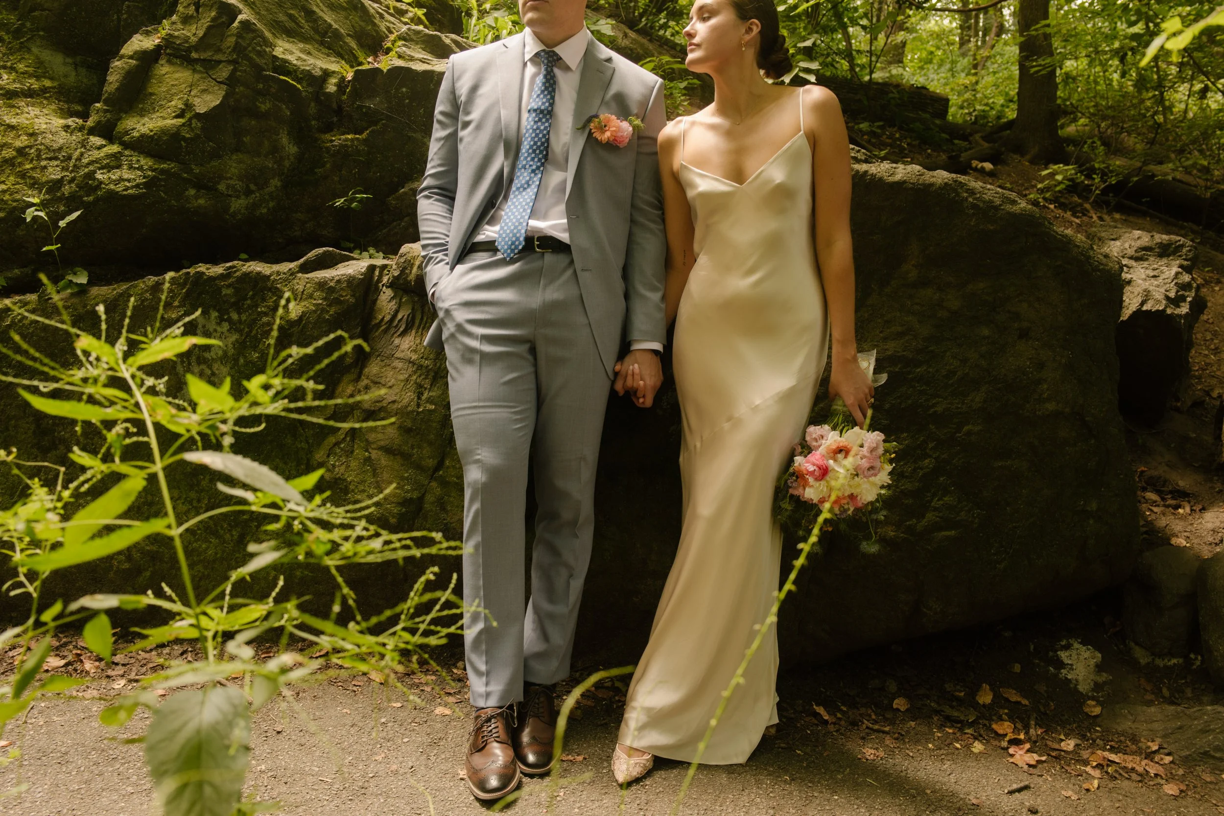 Bride and groom holding hands beside a rocky outcrop during outdoor wedding portraits.