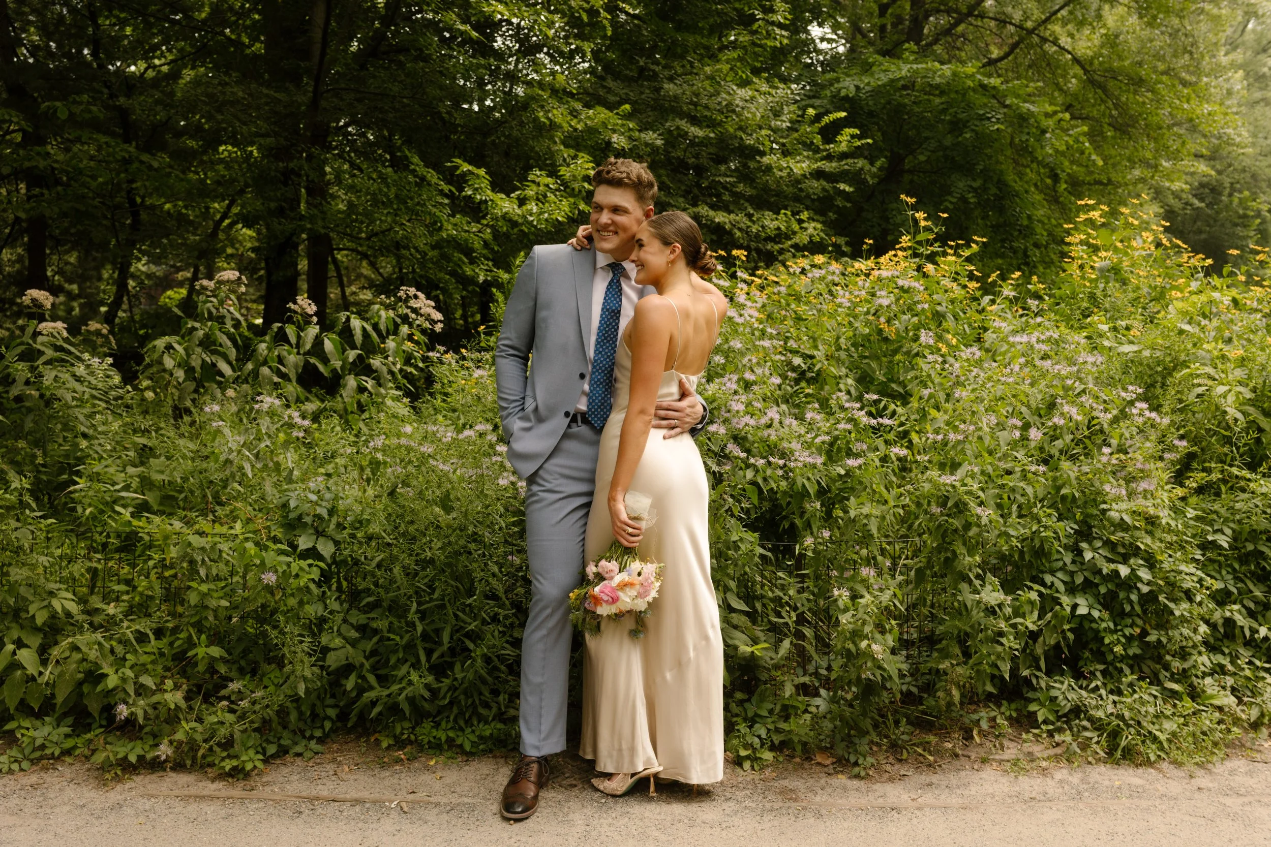 Newlyweds smiling together in a lush Central Park garden during relaxed wedding portraits.