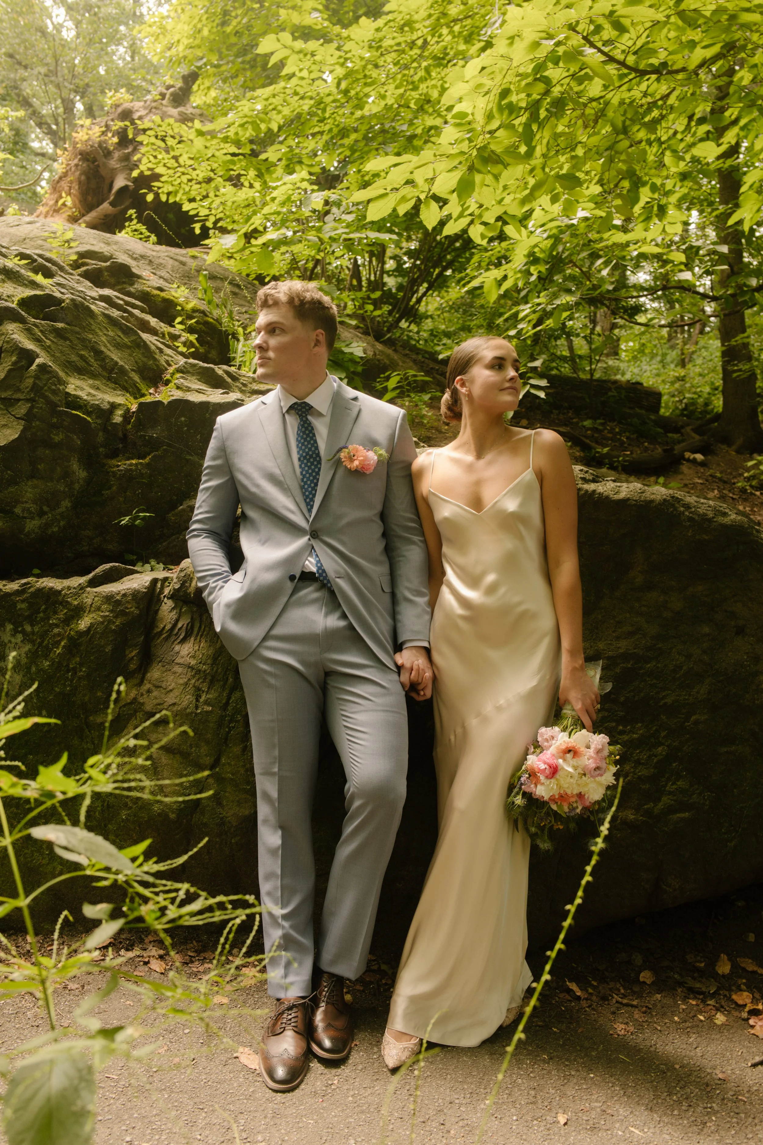 Bride and groom standing together beside large boulders in Central Park during relaxed wedding portraits.