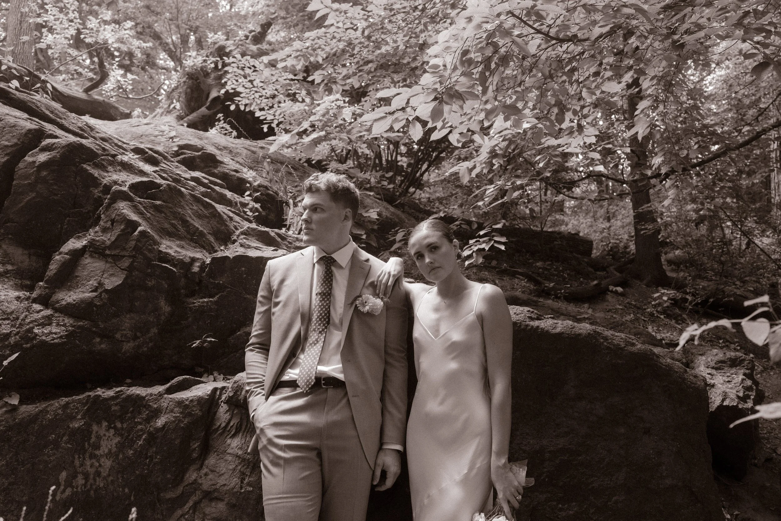 Black-and-white portrait of the bride and groom leaning against a rock formation during outdoor wedding portraits.