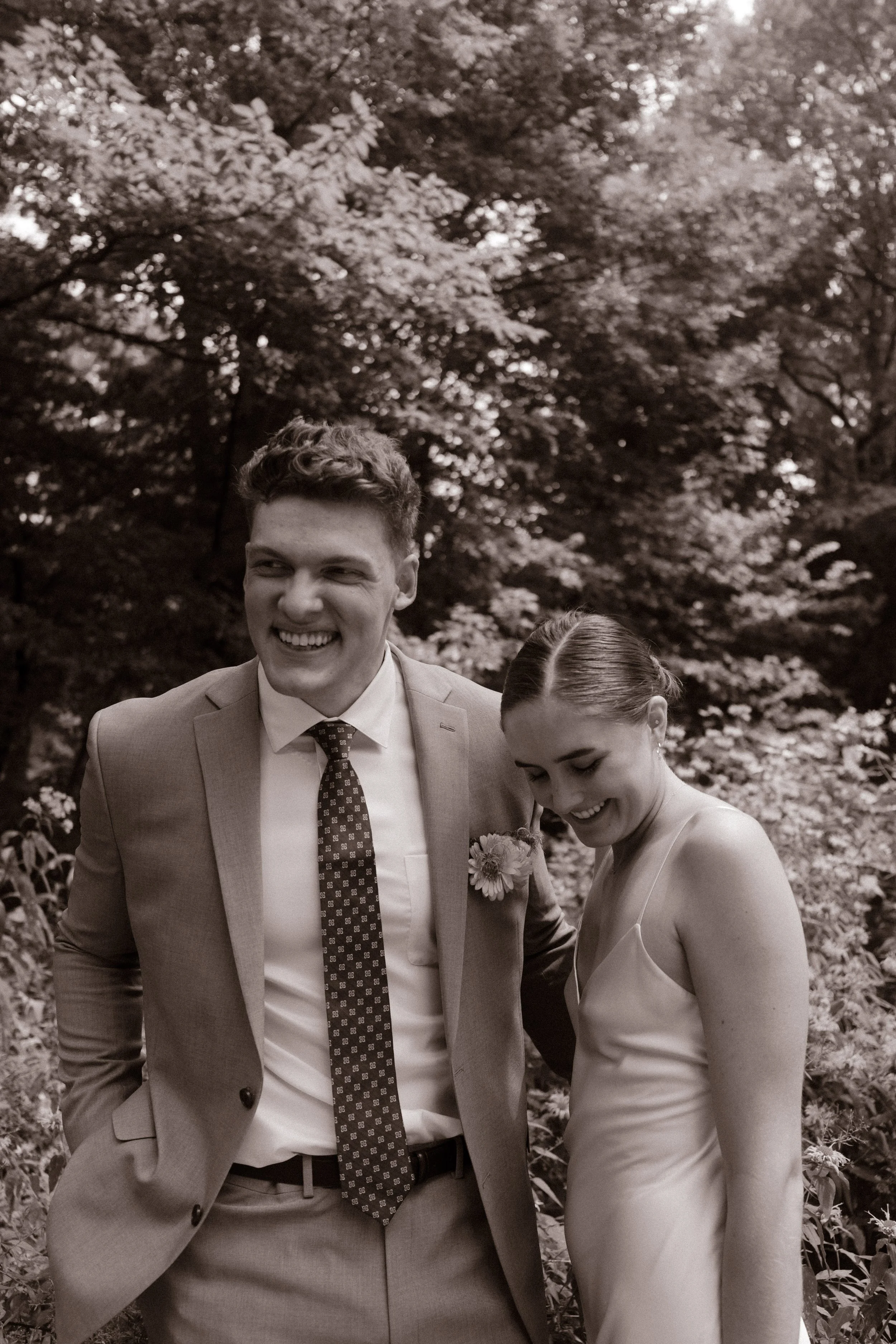 Black-and-white candid of the bride and groom laughing together in Central Park during their wedding day timeline.