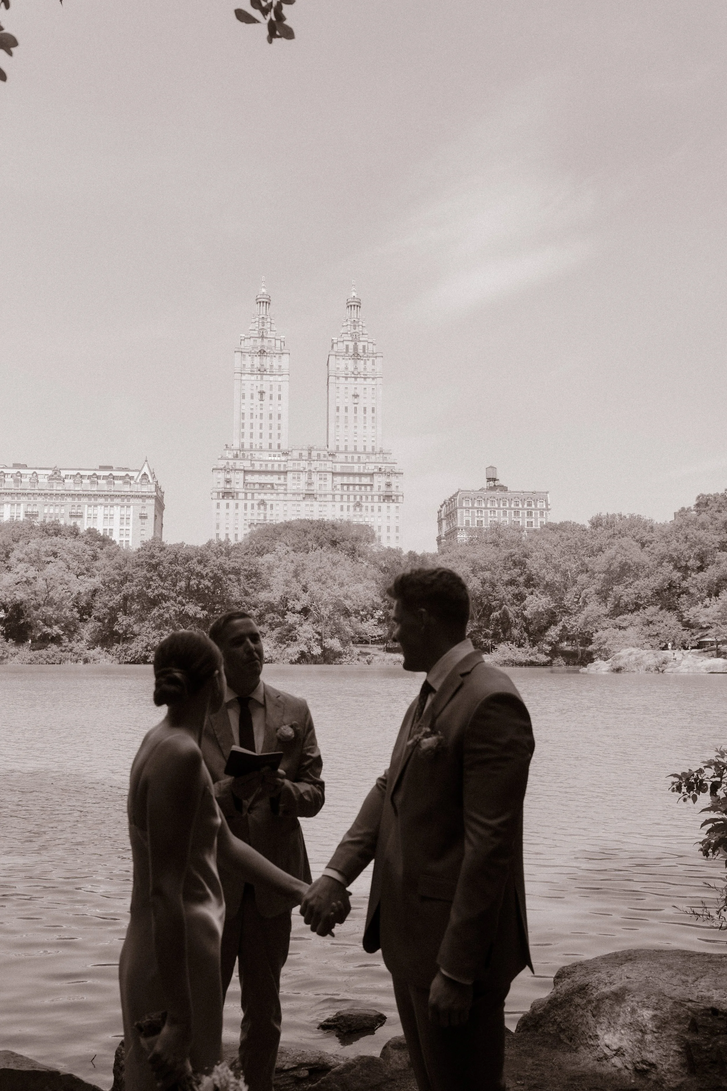 Black-and-white portrait of the bride and groom holding hands during their lakeside ceremony as part of their wedding day timeline.