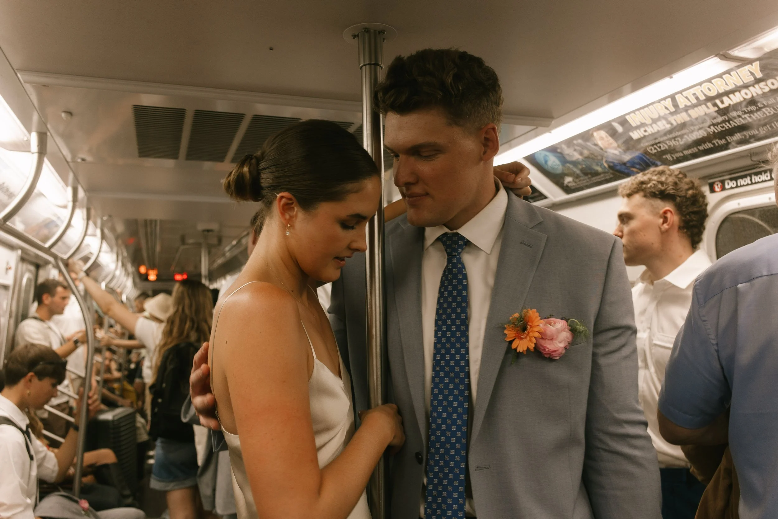 Bride and groom embracing on a crowded New York City subway during a quiet moment in their wedding day timeline.