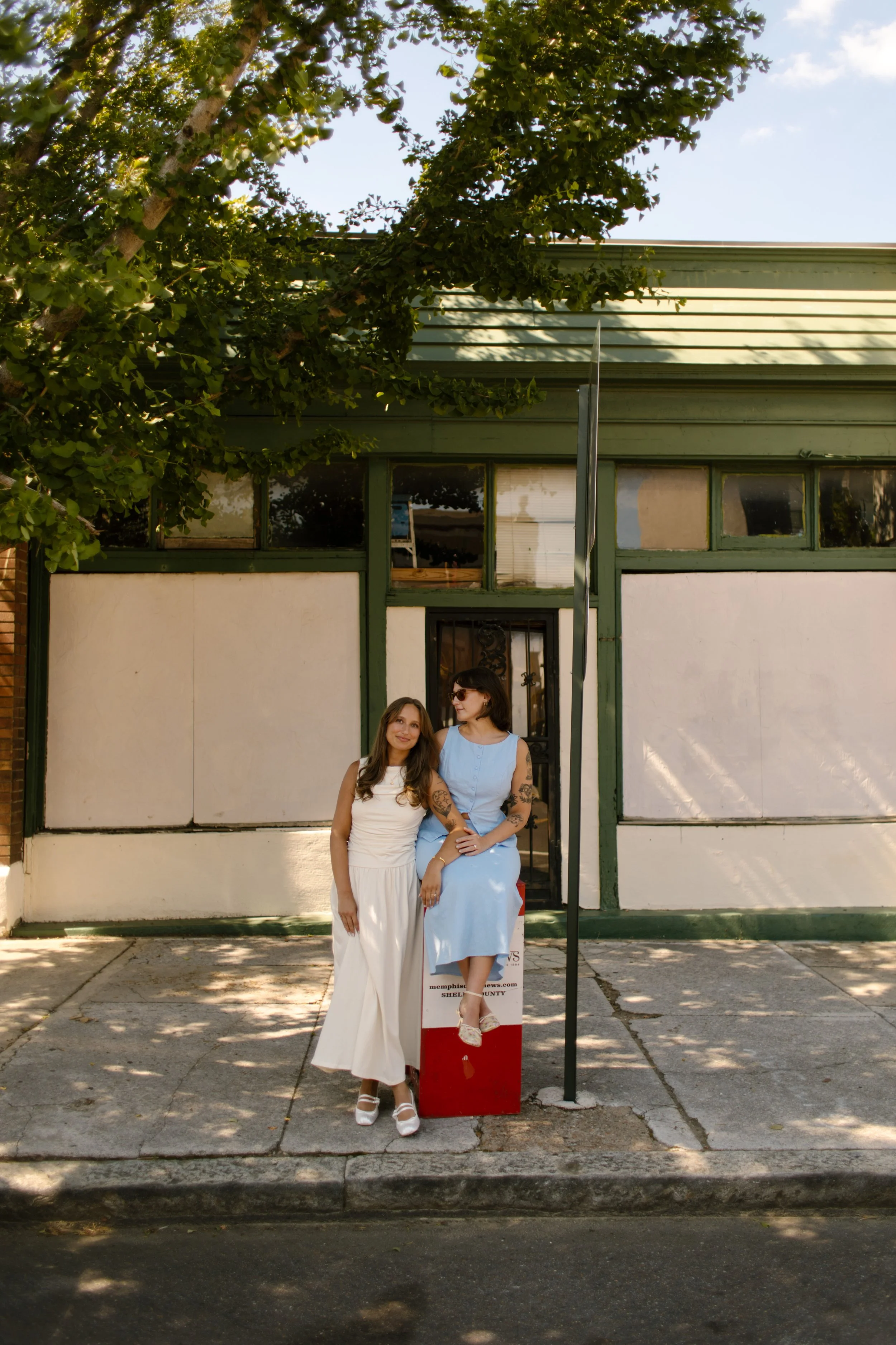 Couple stands together on a red cooler outside a vintage storefront during relaxed wedding portraits.