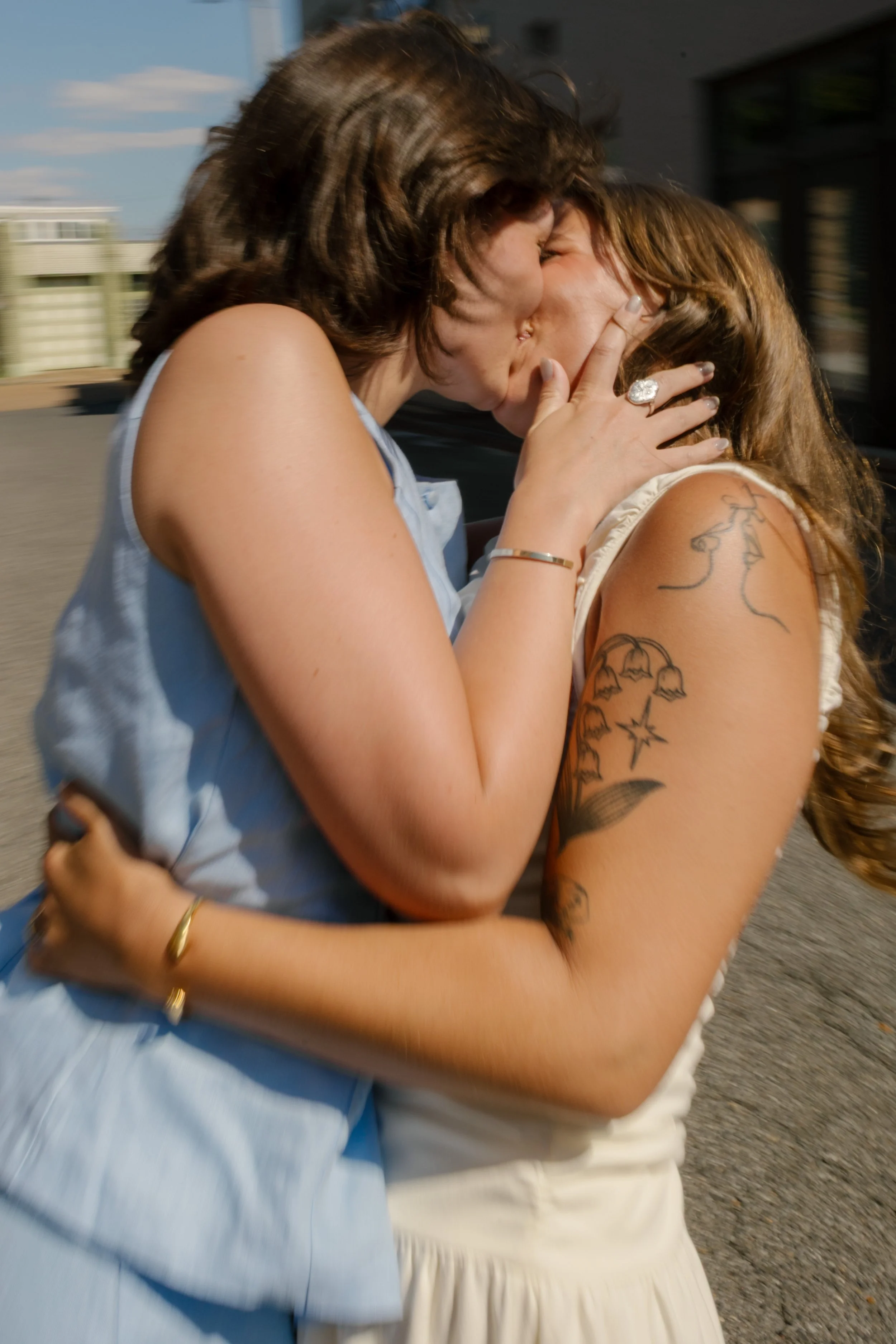 Close-up of two brides sharing a kiss in bright afternoon sunlight.