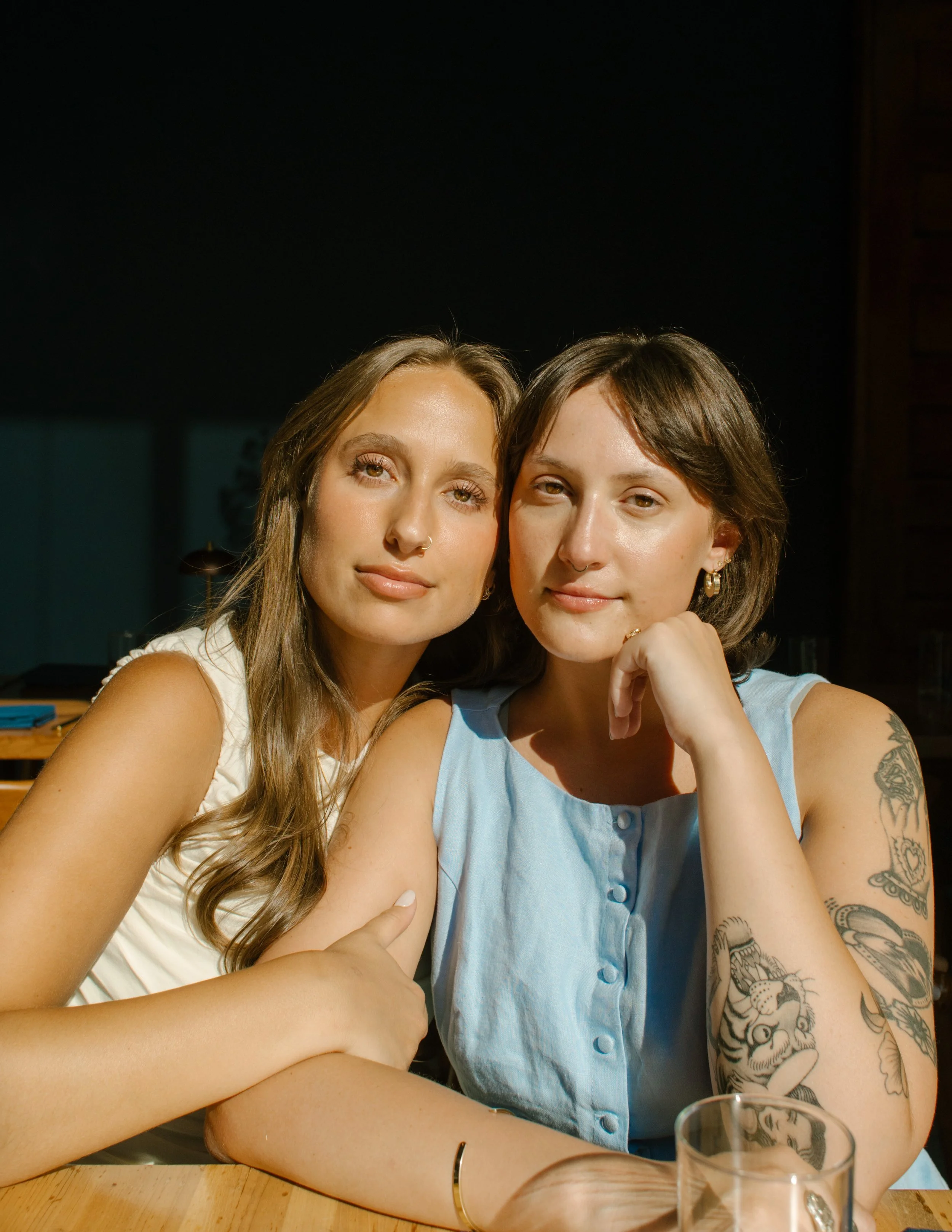 Natural window-lit portrait of two newlyweds seated together inside a restaurant.